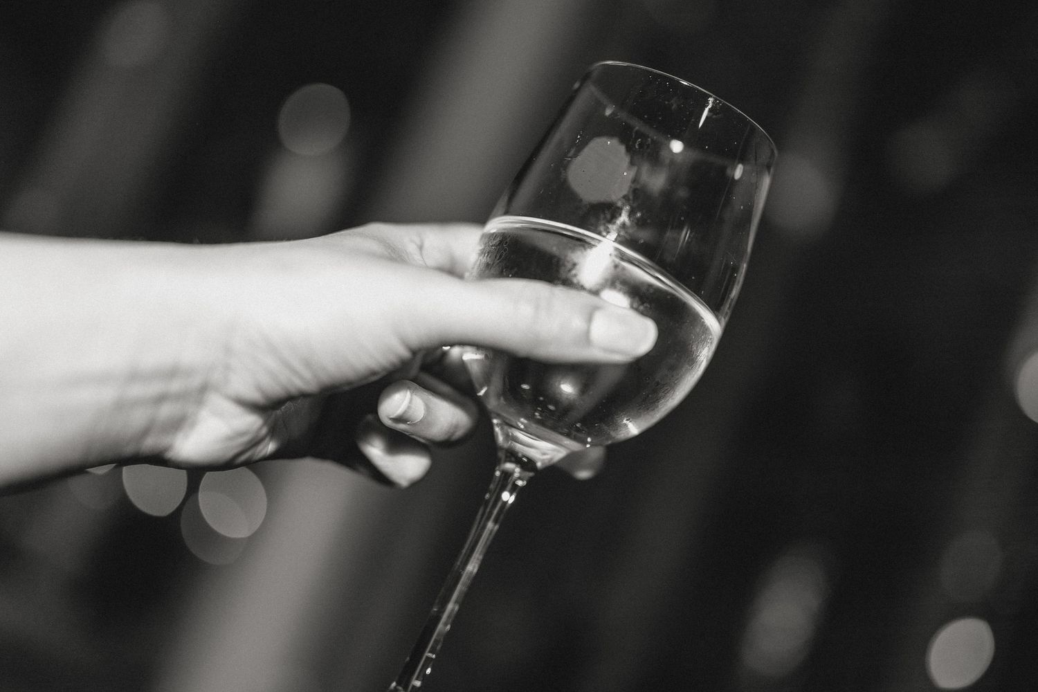 Black and white close-up of hands holding wine glasses at an event.