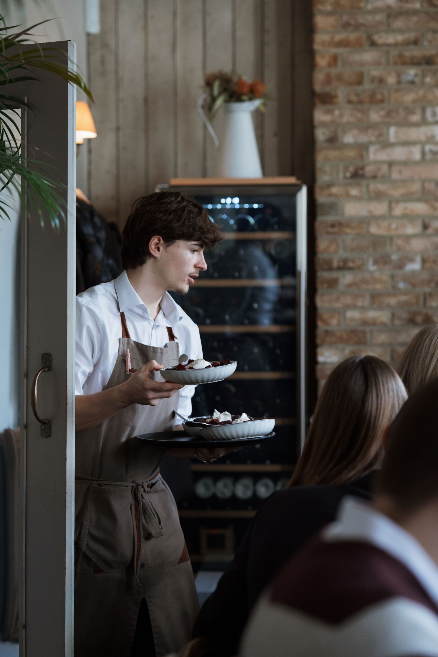 Restaurant staff serving guests in an intimate brick-walled dining space.