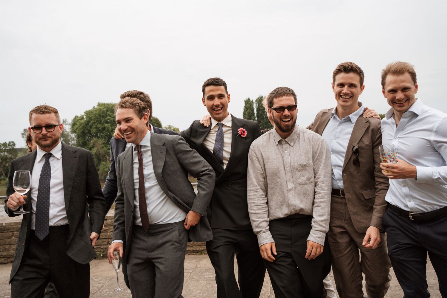 Groomsmen in suits and ties pose casually together outdoors.