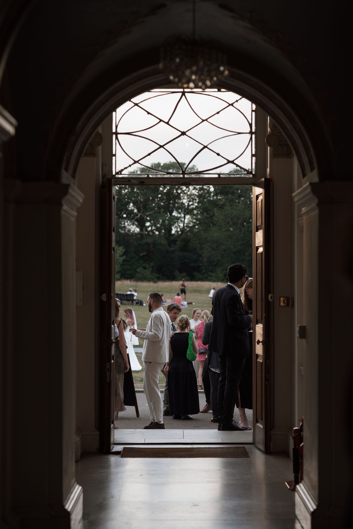 View through an arched hallway showing wedding guests gathered outside.