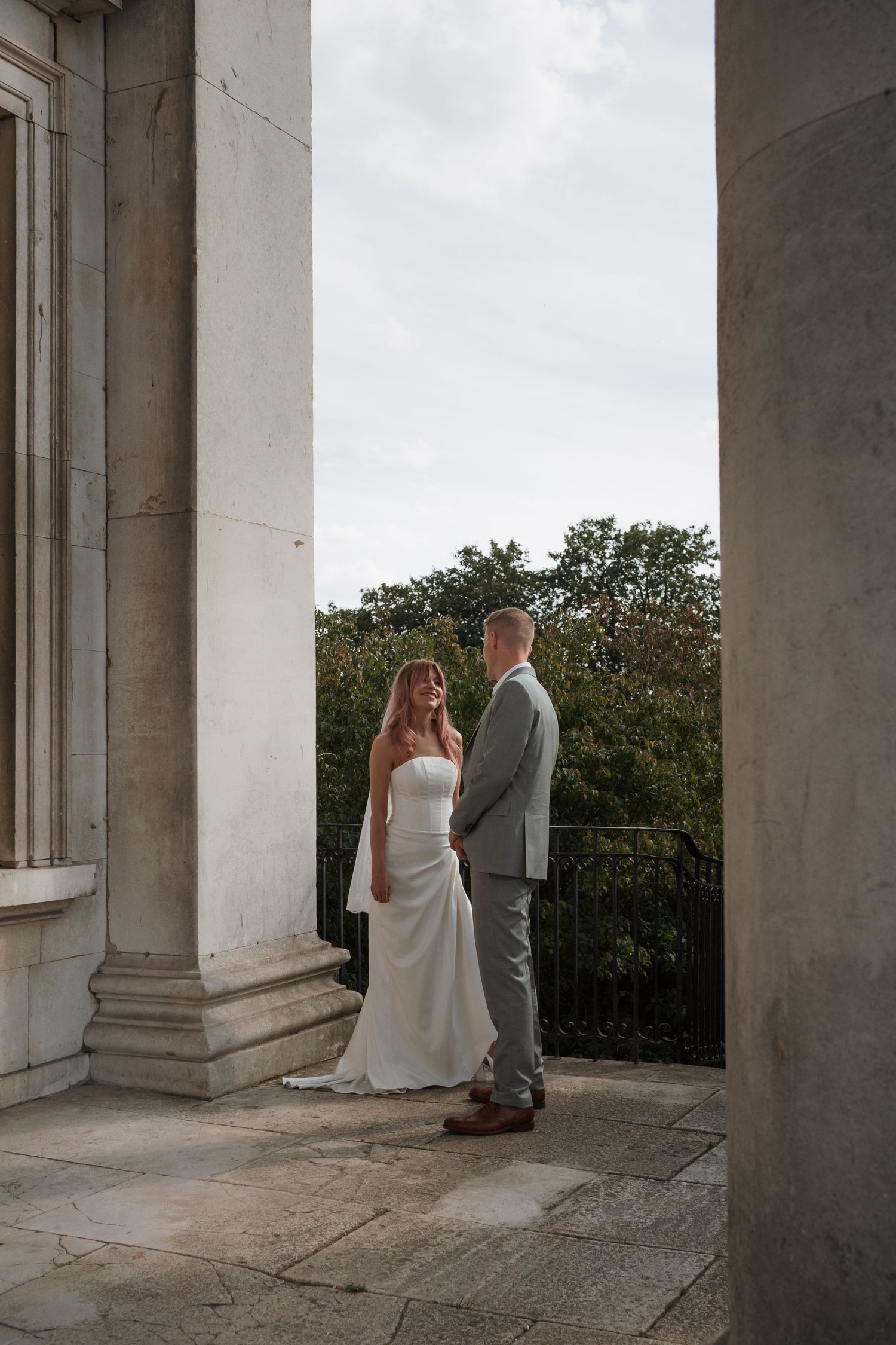 Wedding couple photographed between white stone columns of a classical building.