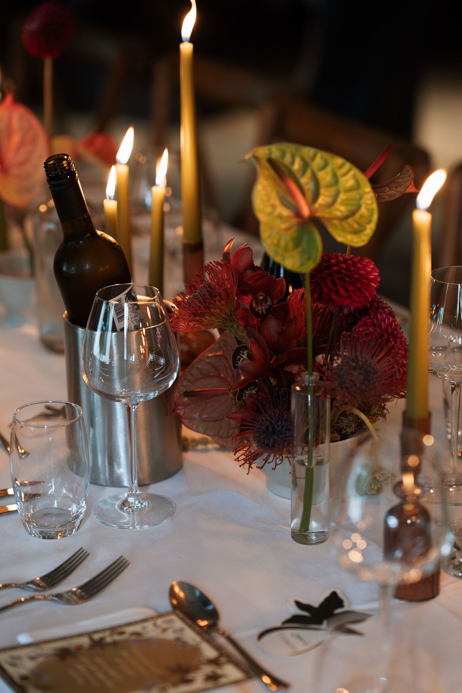 Intimate table setting with red flowers, candles and wine glasses on white tablecloth.