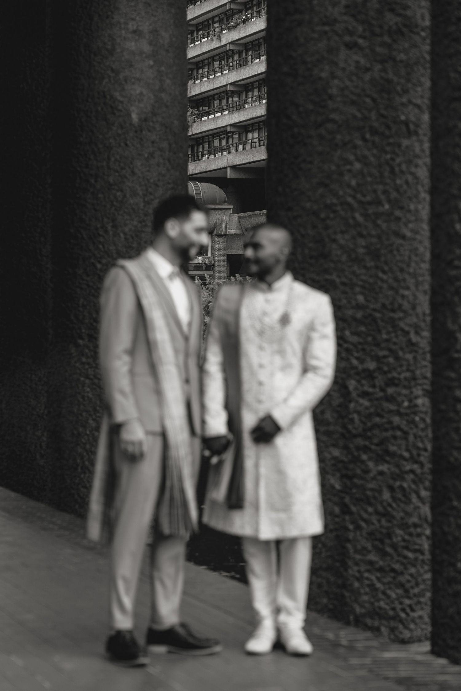 Black and white portrait of two people in formal attire standing under architectural columns.