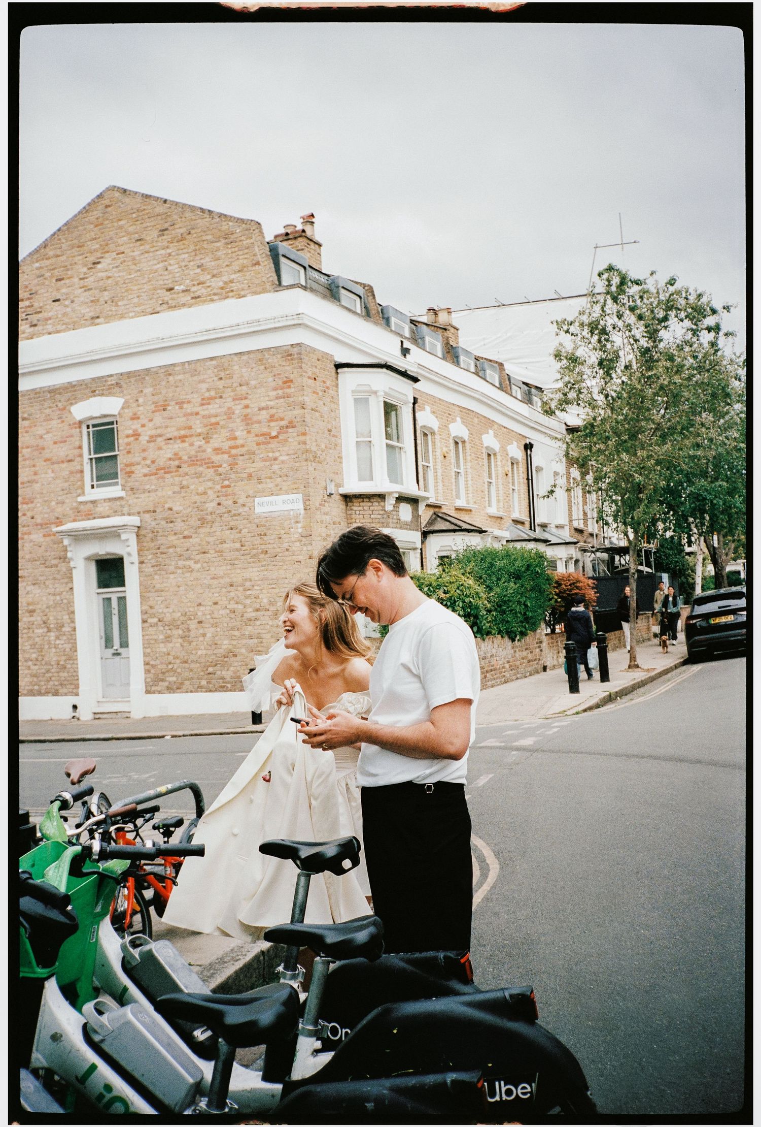 Couple sharing a romantic moment on a London street beside Uber bikes, woman in white dress, film photography style.