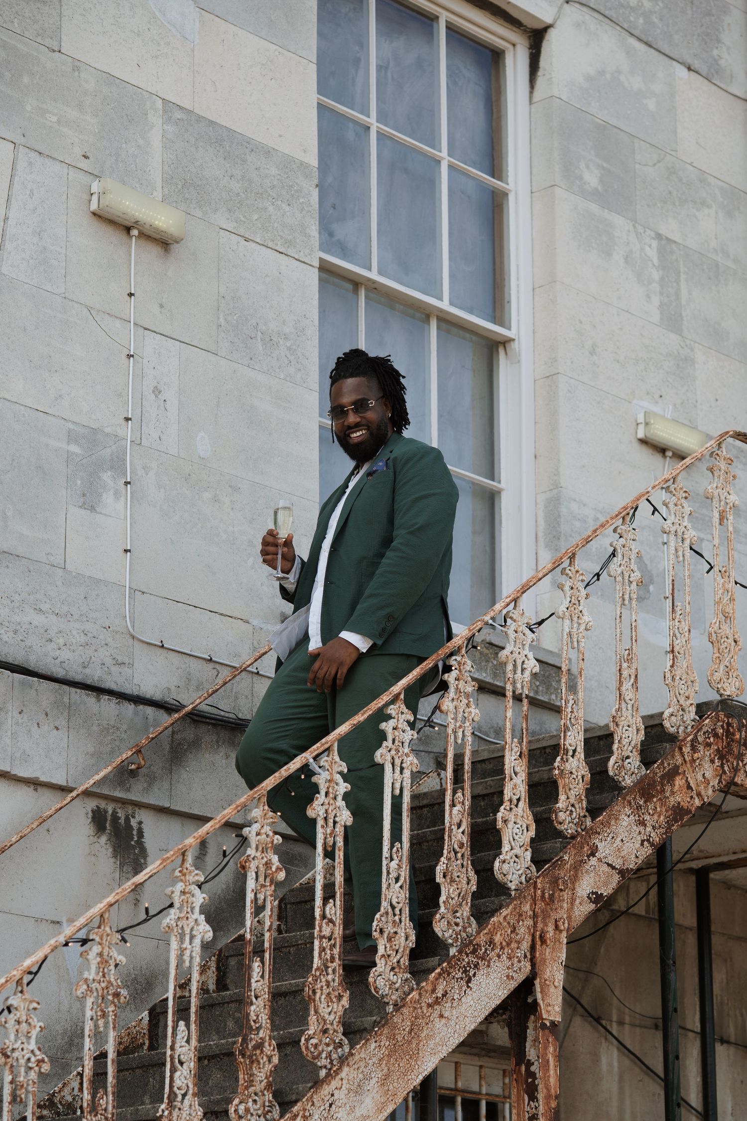 Person in green suit poses on ornate stone staircase with decorative railing.