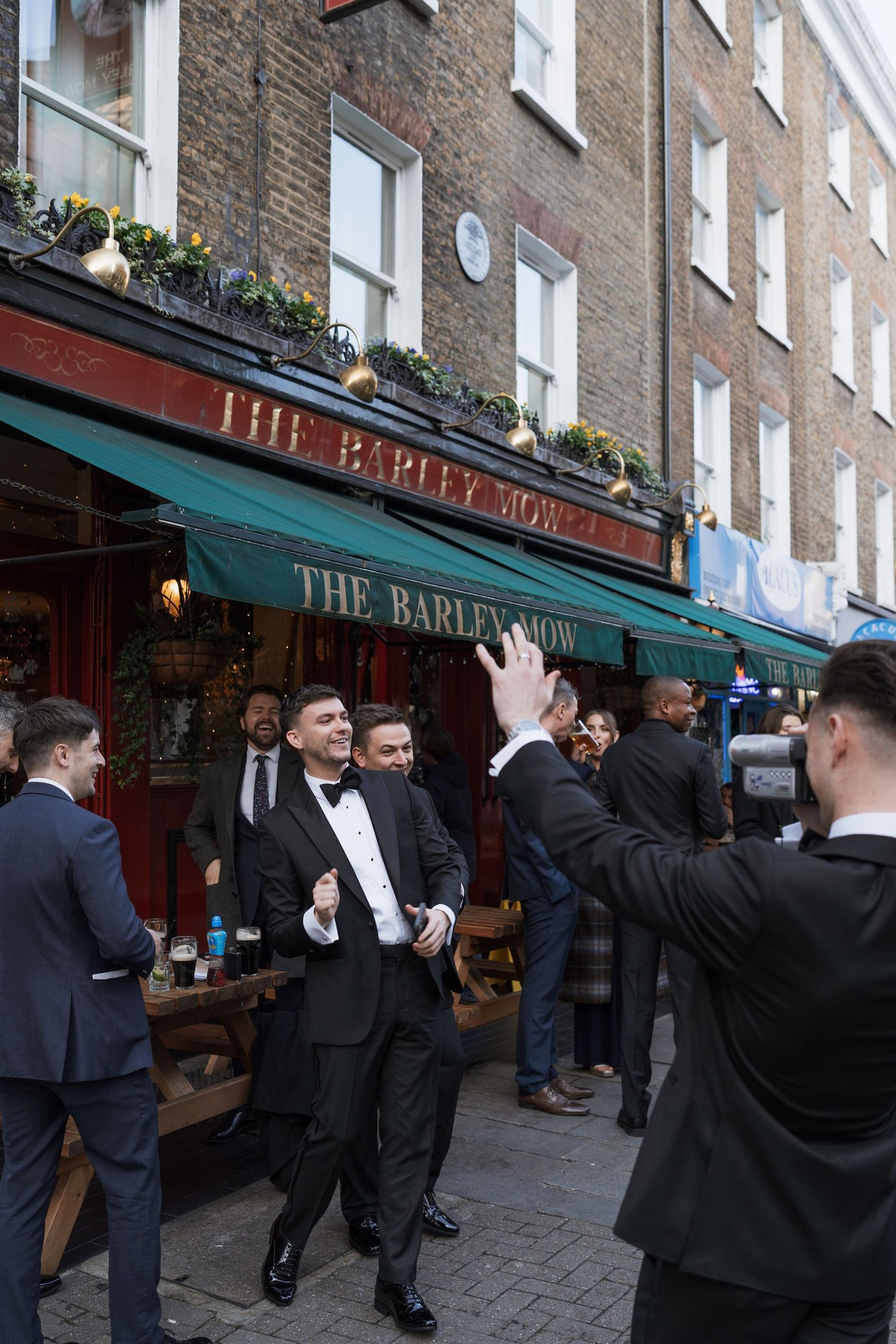People in formal attire gathered outside The Barley Mow pub in London.