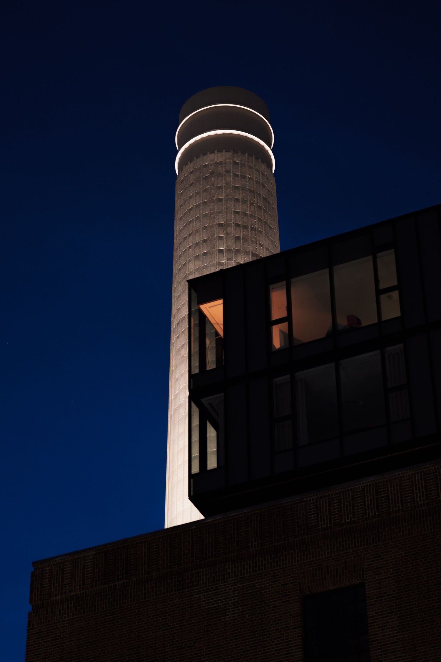 Silhouette of industrial buildings and a tower against dark blue sky.