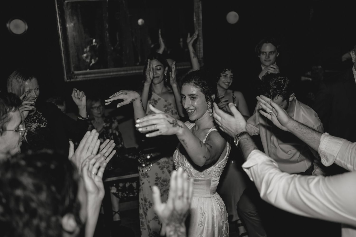 Black and white photo of party guests with raised hands dancing at a celebration.
