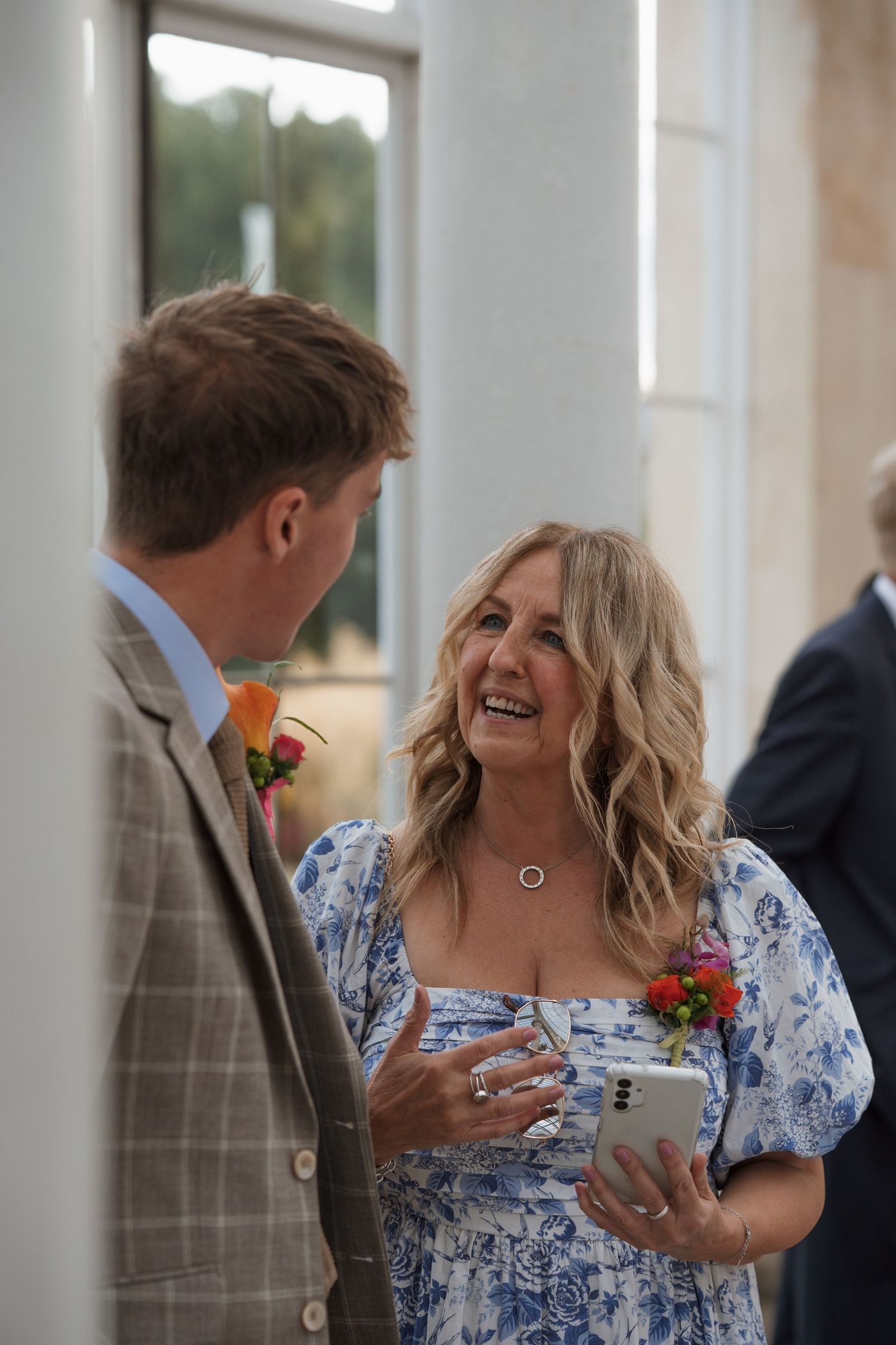 Wedding guests enjoying conversation during reception in bright conservatory setting.