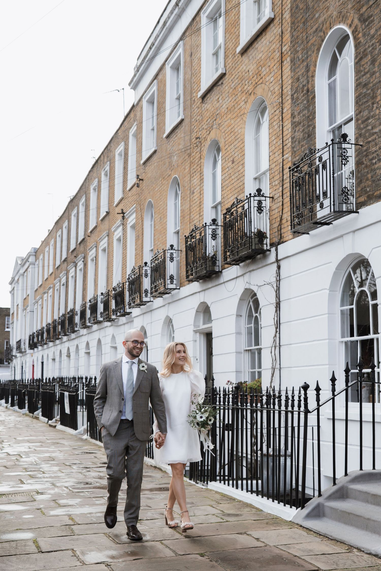 A couple walking along a beautiful Georgian terrace with white facades and black railings.