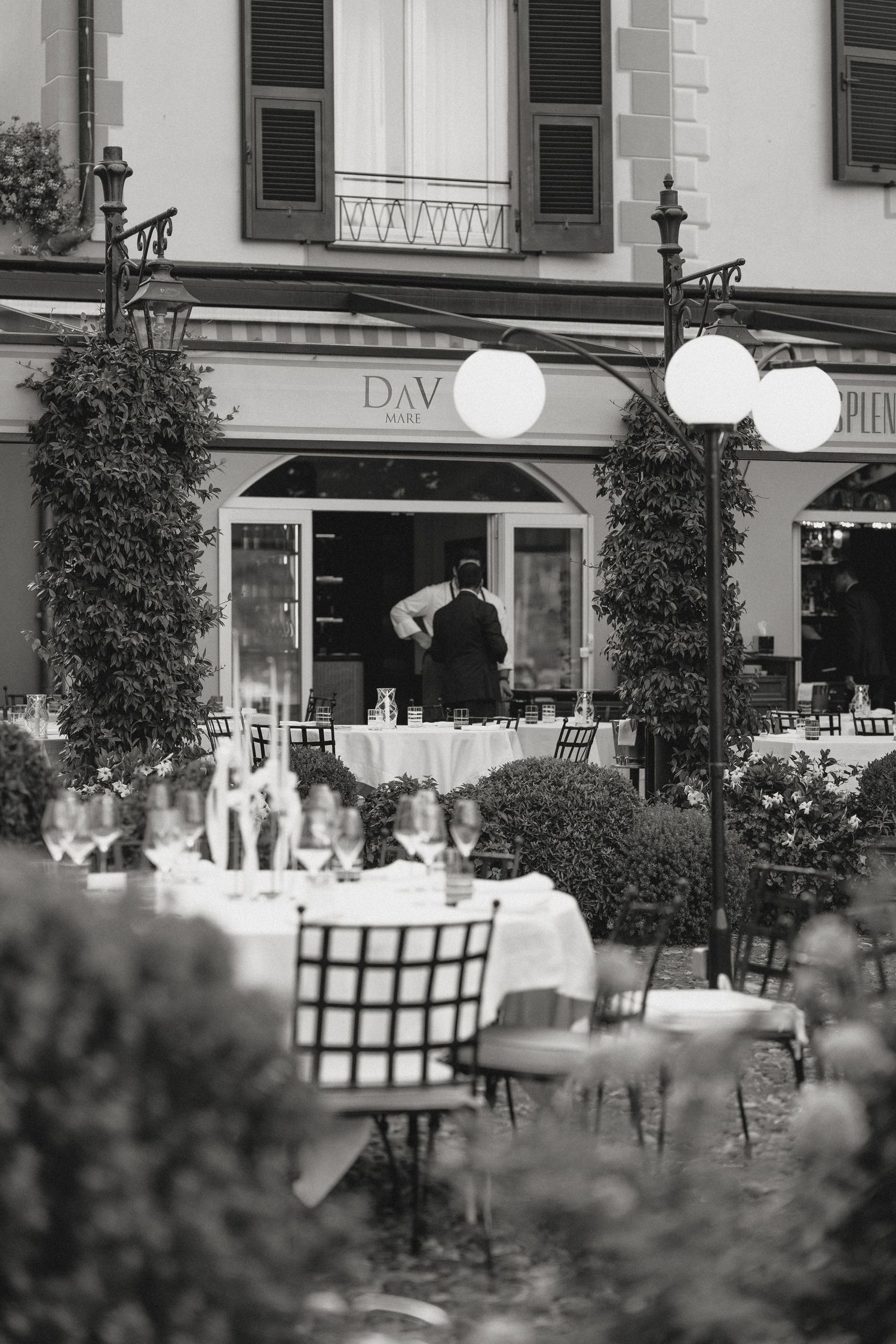 Black and white view of an outdoor restaurant terrace with white tablecloths and chairs.