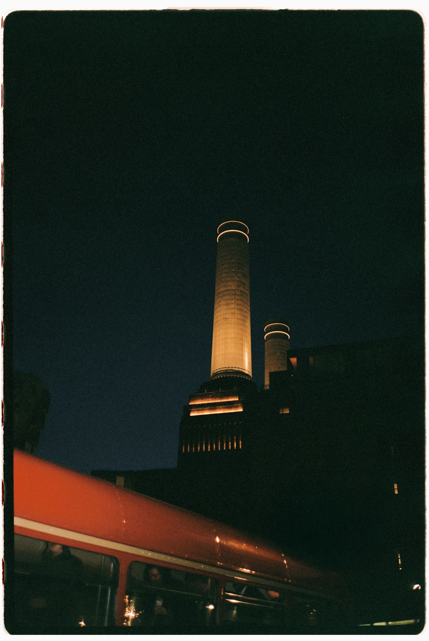 Illuminated industrial smokestacks against a dark night sky.