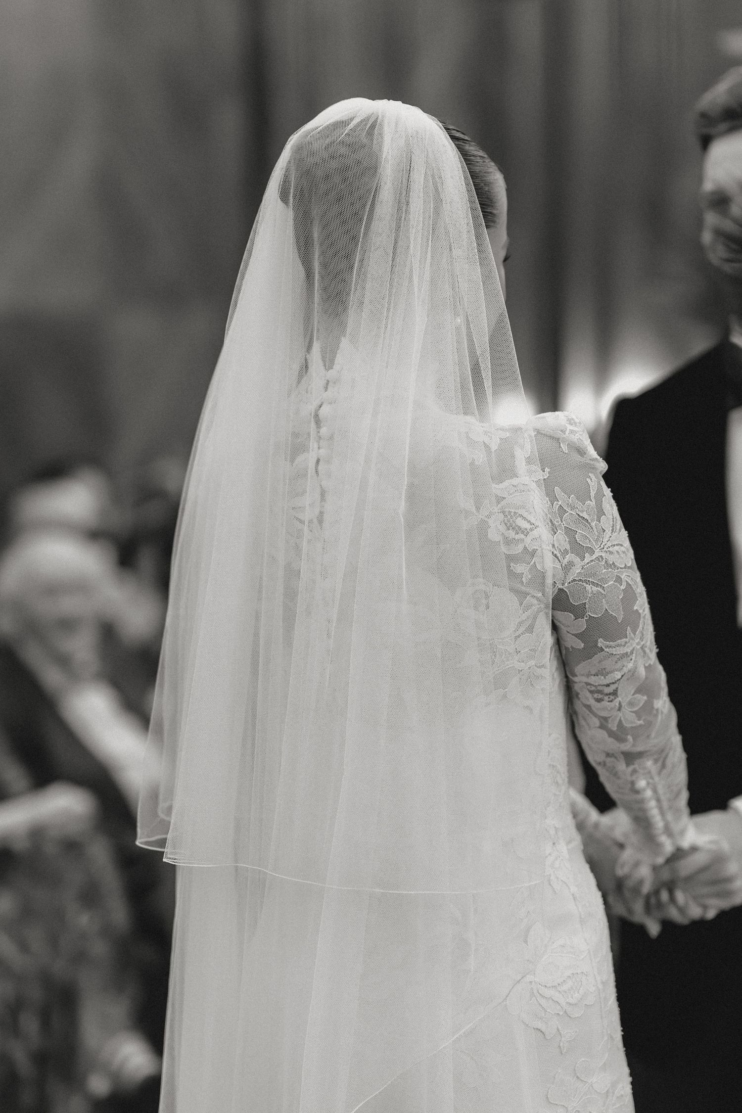 Back view of a bride wearing a long lace veil during a wedding ceremony.