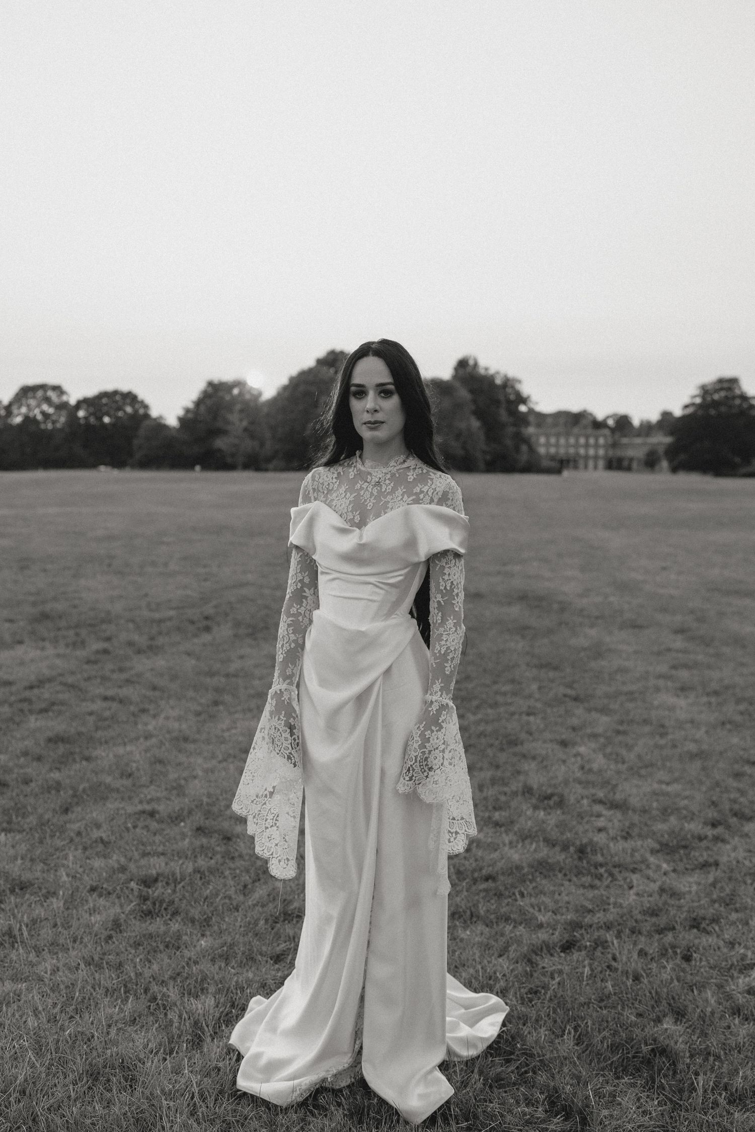 A vintage-inspired bridal portrait in a flowing white lace dress against an open field.