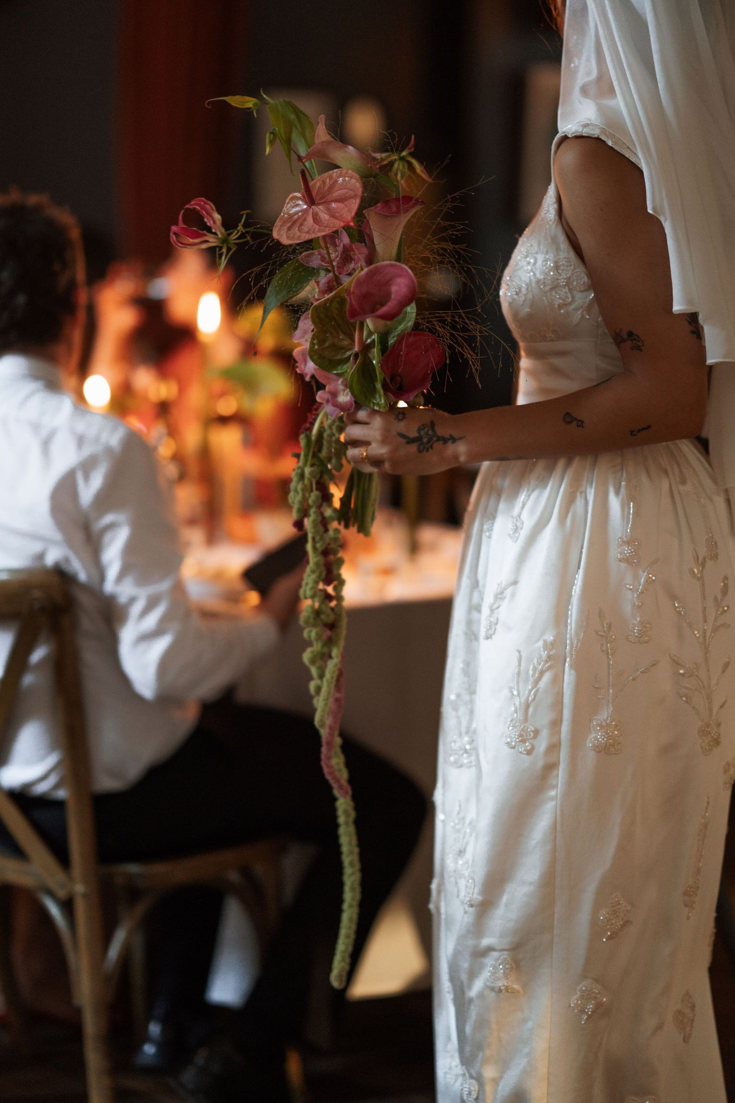 Person in white dress holding pink floral bouquet at evening event.