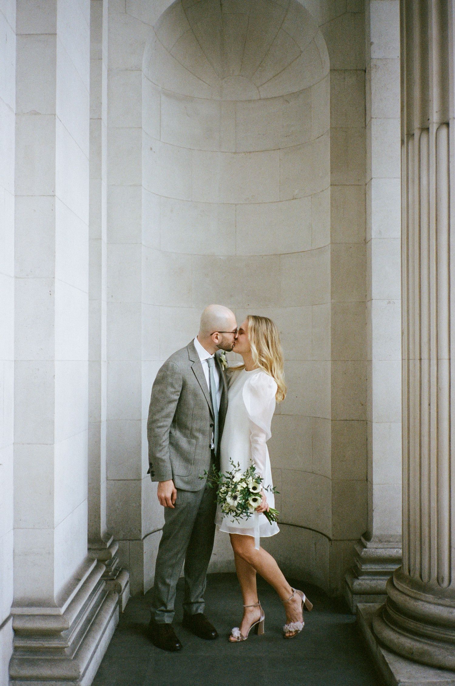 Romantic couple portraits between elegant white stone columns in classic architecture.
