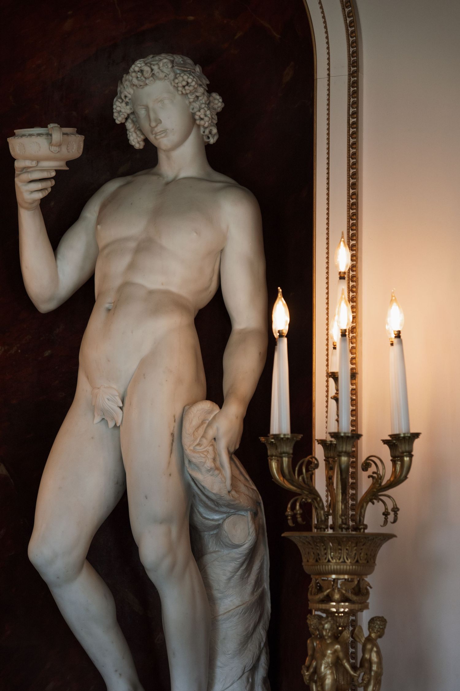 Classical marble statue illuminated by candlelight in an ornate interior setting.
