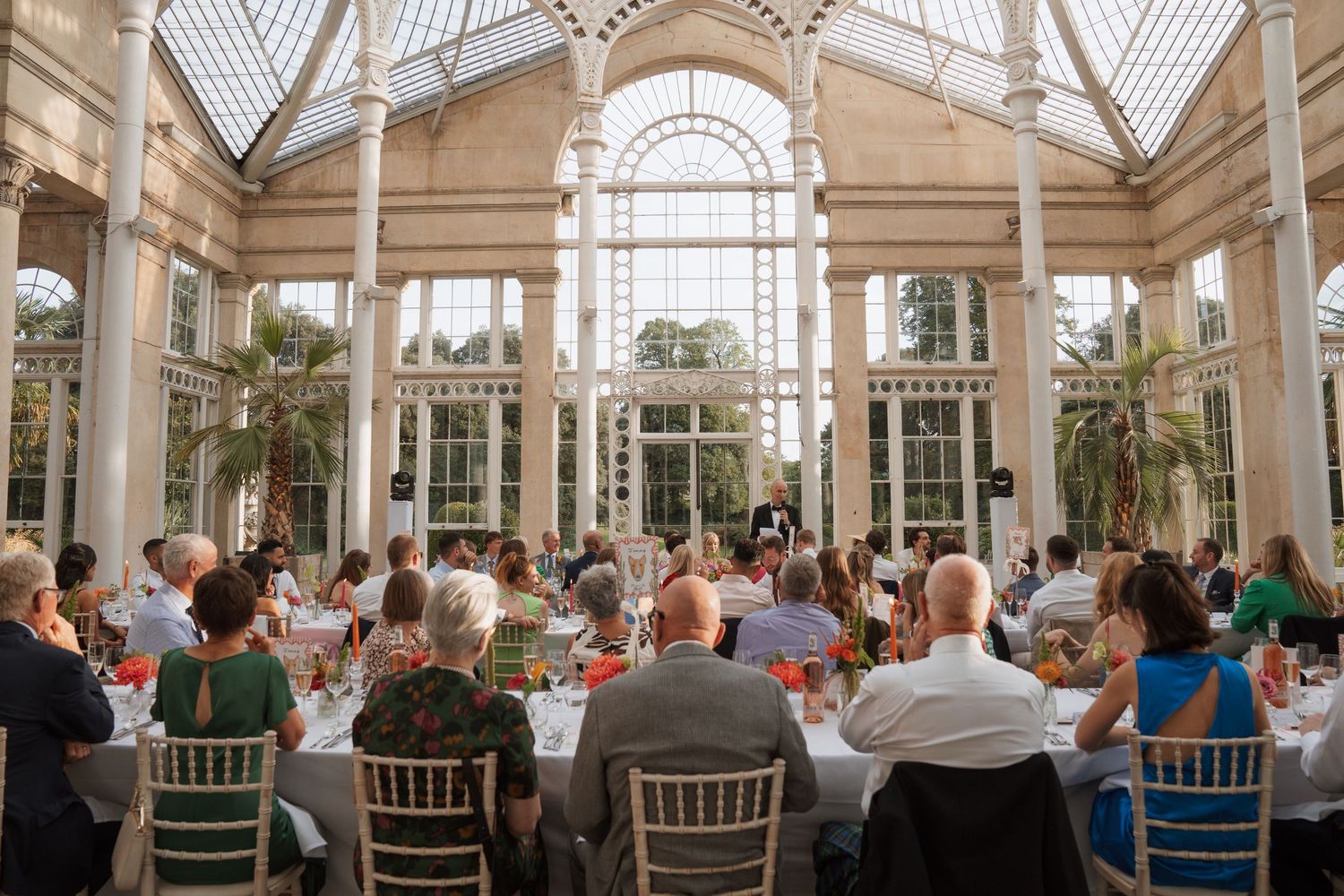 Wide-angle shot of a bright conservatory filled with wedding guests during a reception.