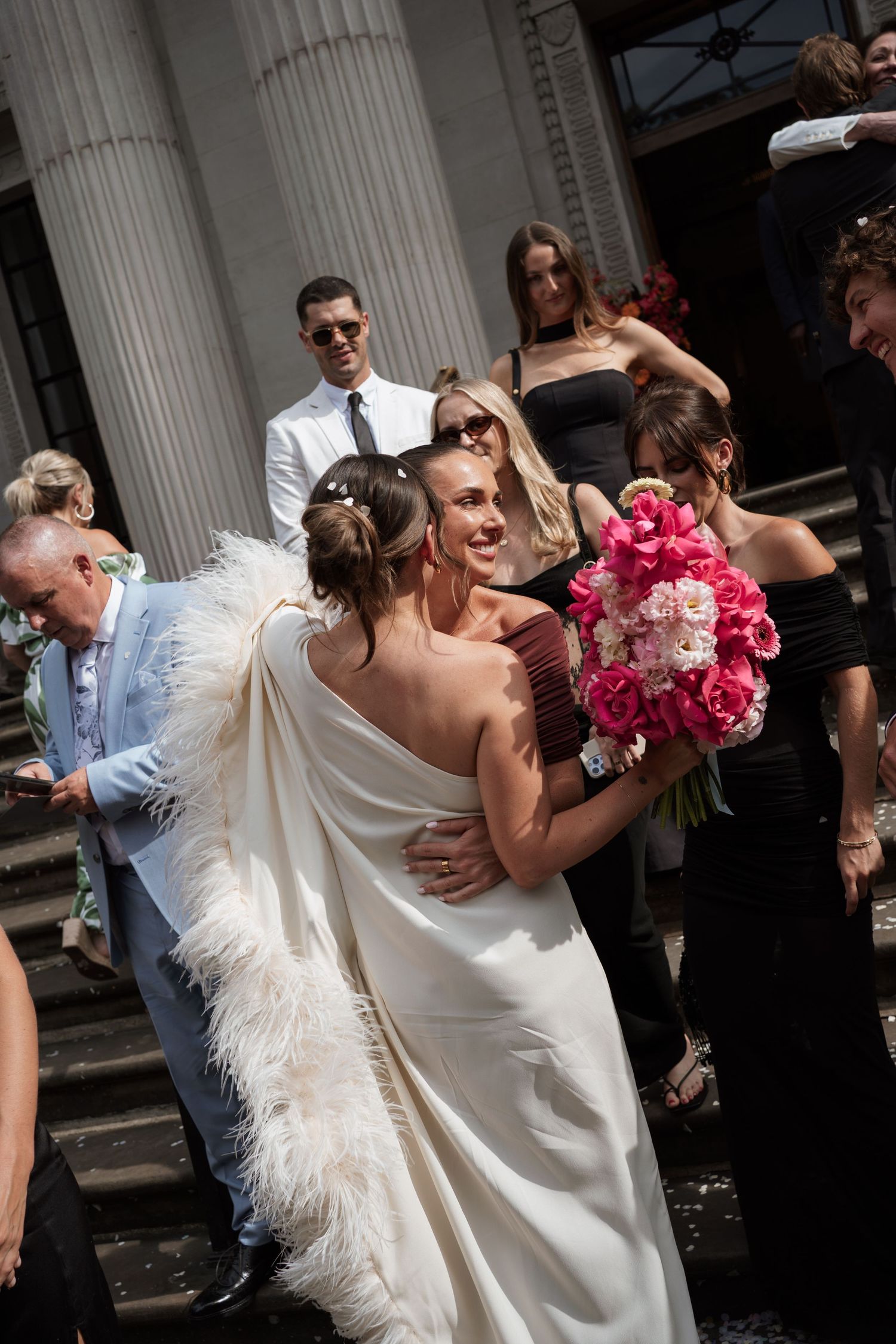 A joyful wedding moment with the bride in a white feathered dress holding pink bouquet during the celebration.