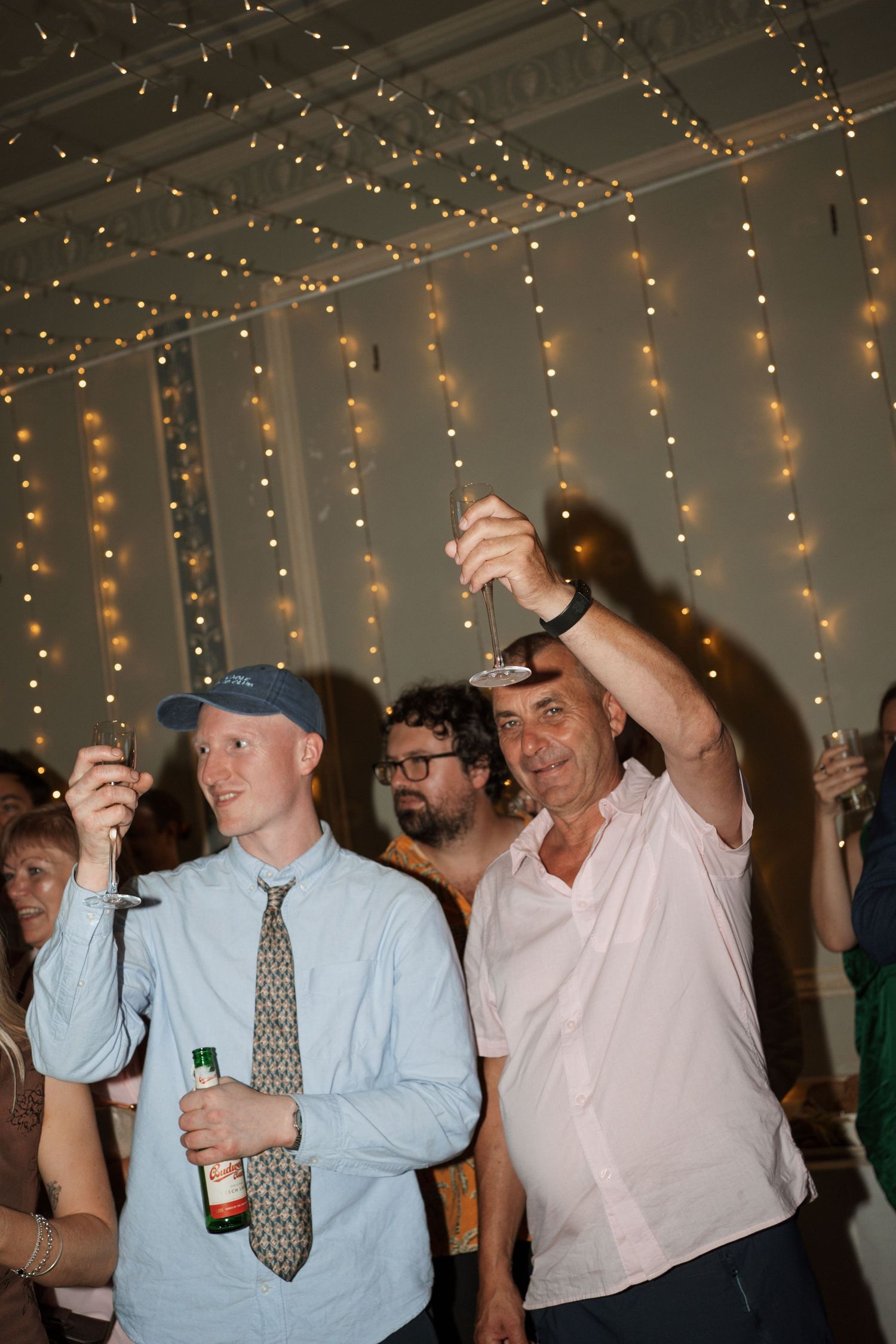 Party guests dance under hanging string lights at a celebration.