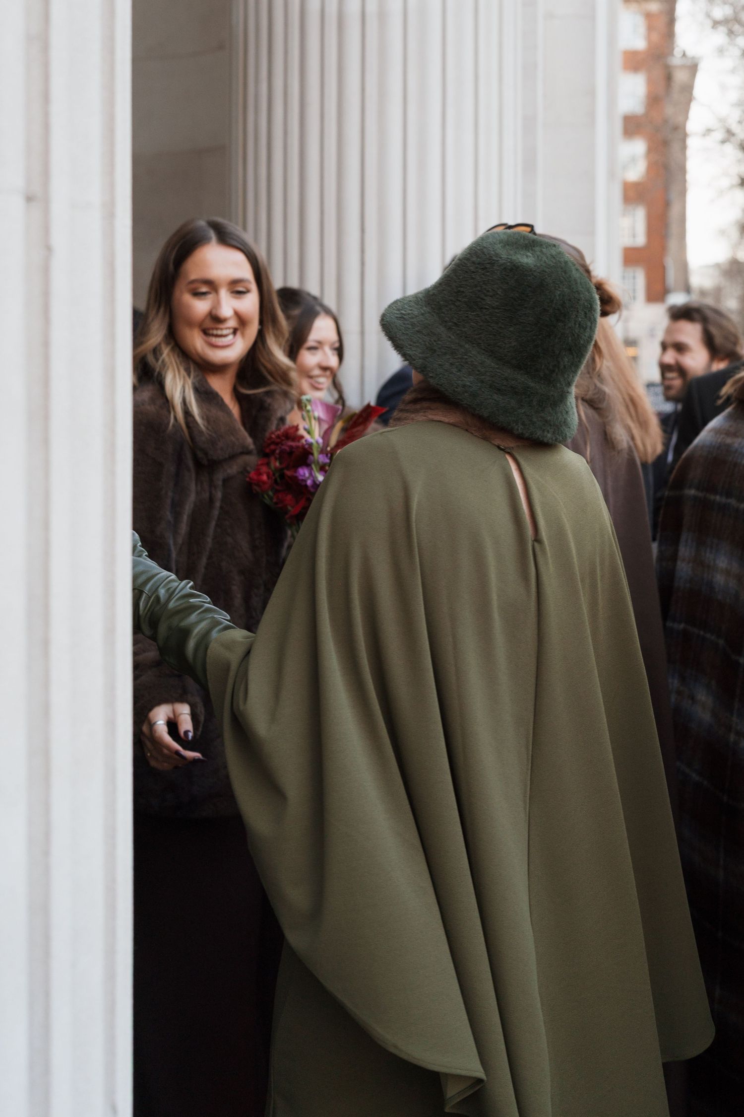 People in coats standing between white classical columns.