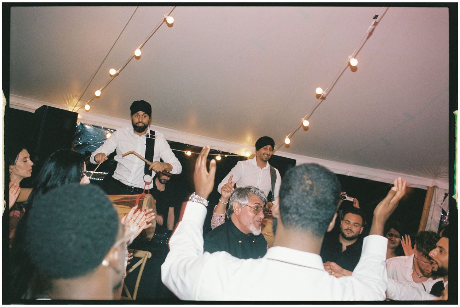 Wedding reception dance floor with guests celebrating under string lights.