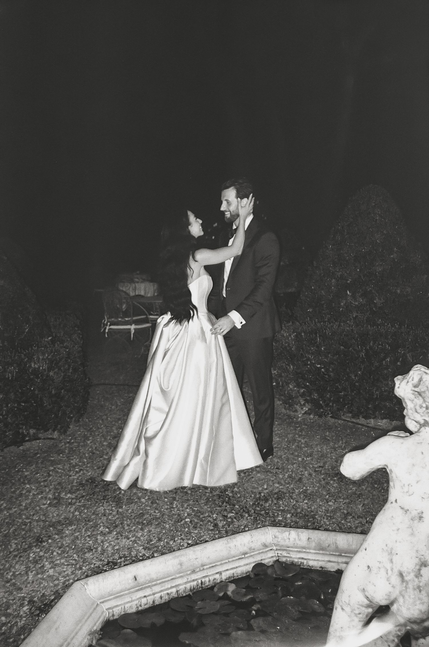 Dramatic black and white nighttime wedding photos near a garden pool.