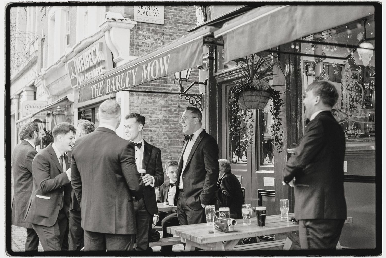 Vintage-style black and white photo of formal event guests outside urban storefronts.