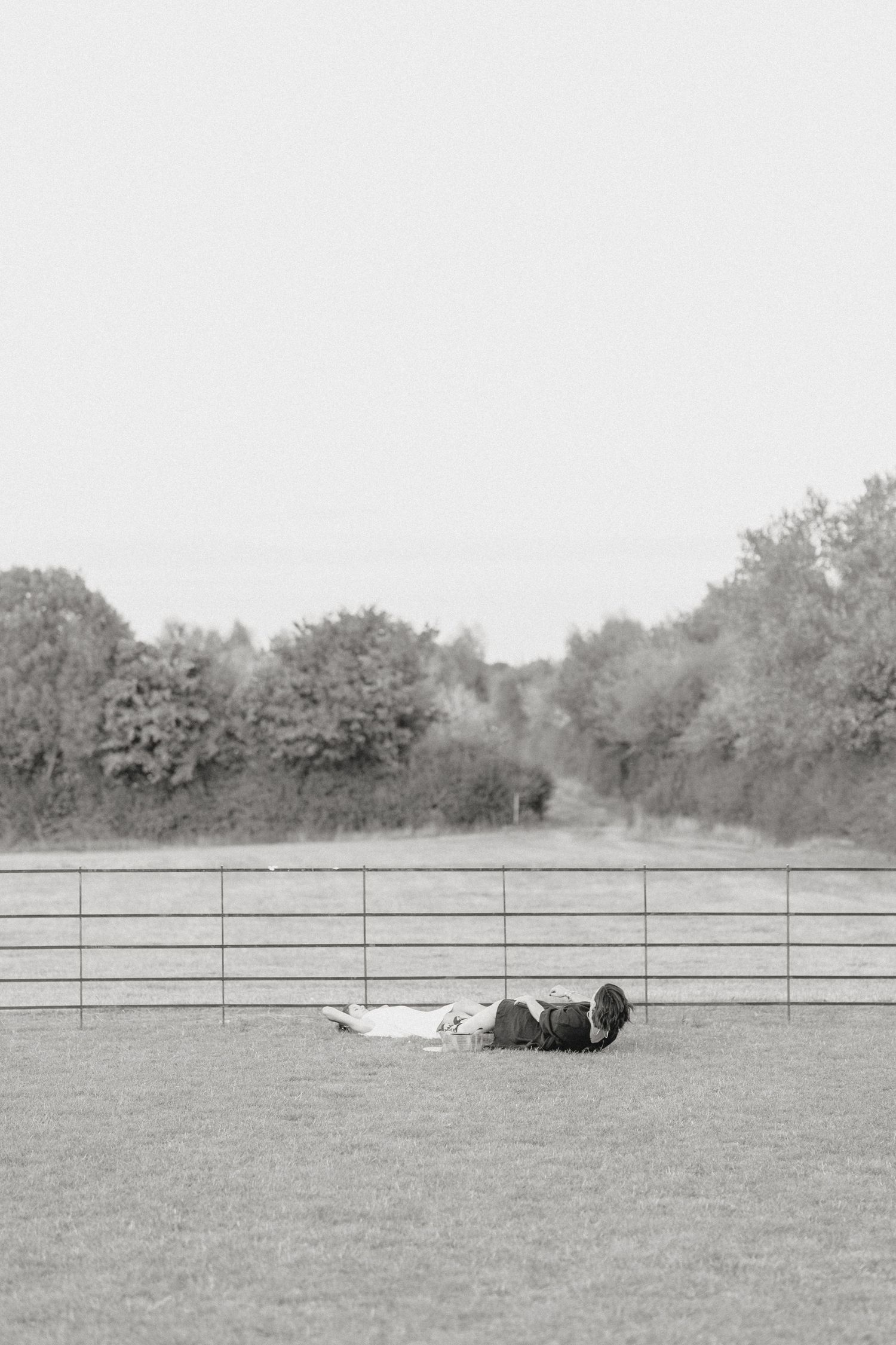 People lying down in a grassy field with fencing in the background.