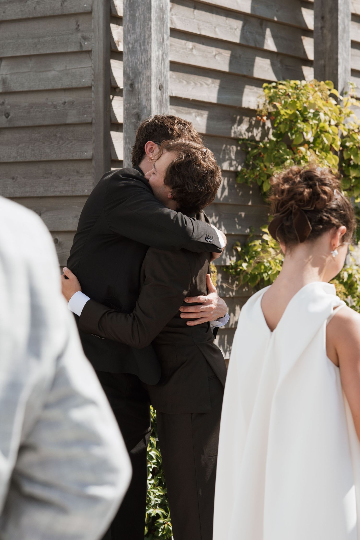 Intimate moment captured during wedding ceremony against wooden wall backdrop.