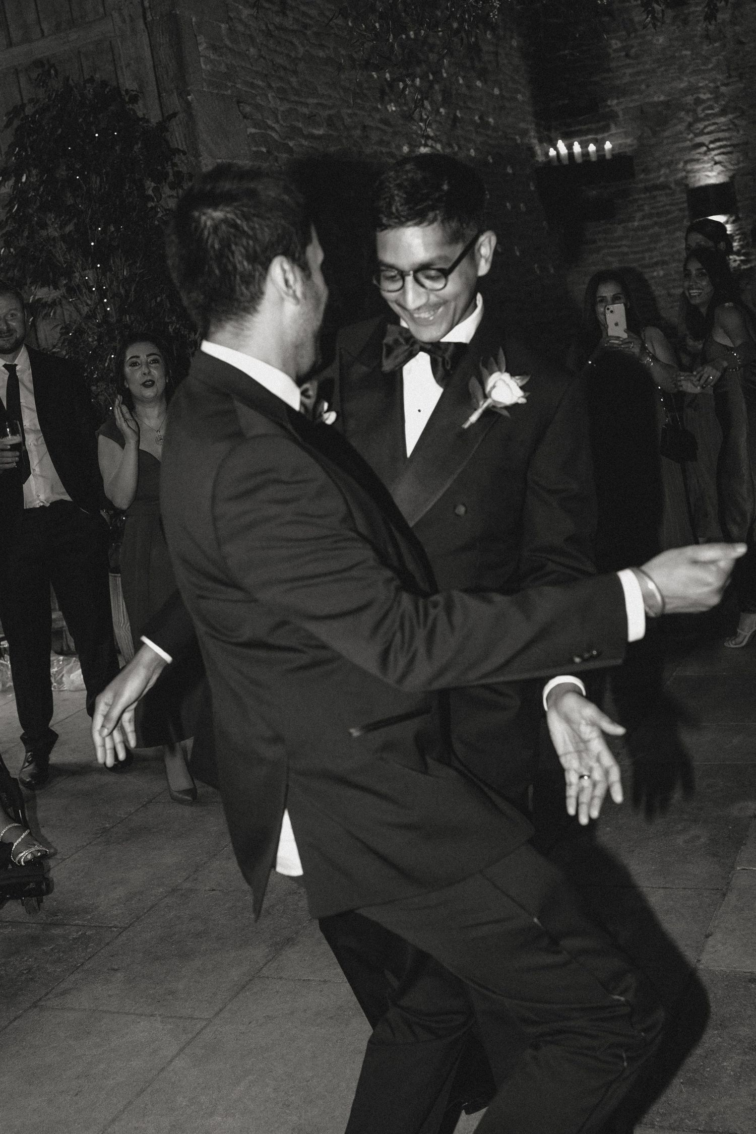 Wedding guests dance energetically in formal attire at a reception party.