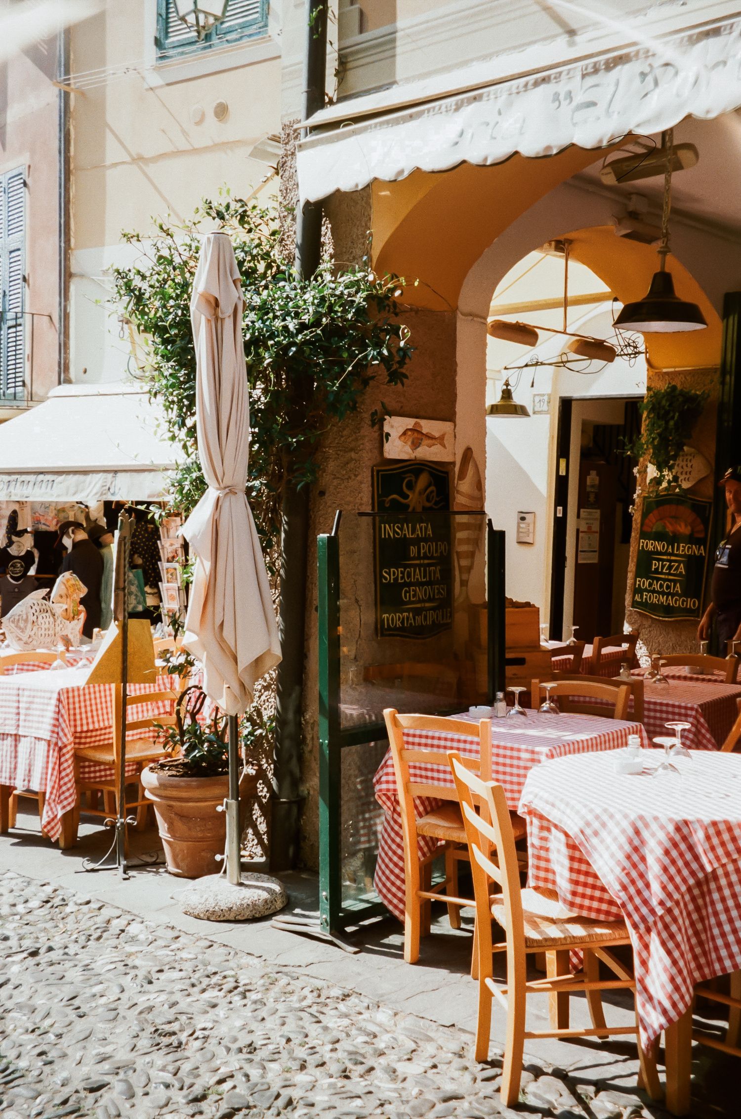 Charming Italian restaurant terrace with red checkered tablecloths and potted plants.