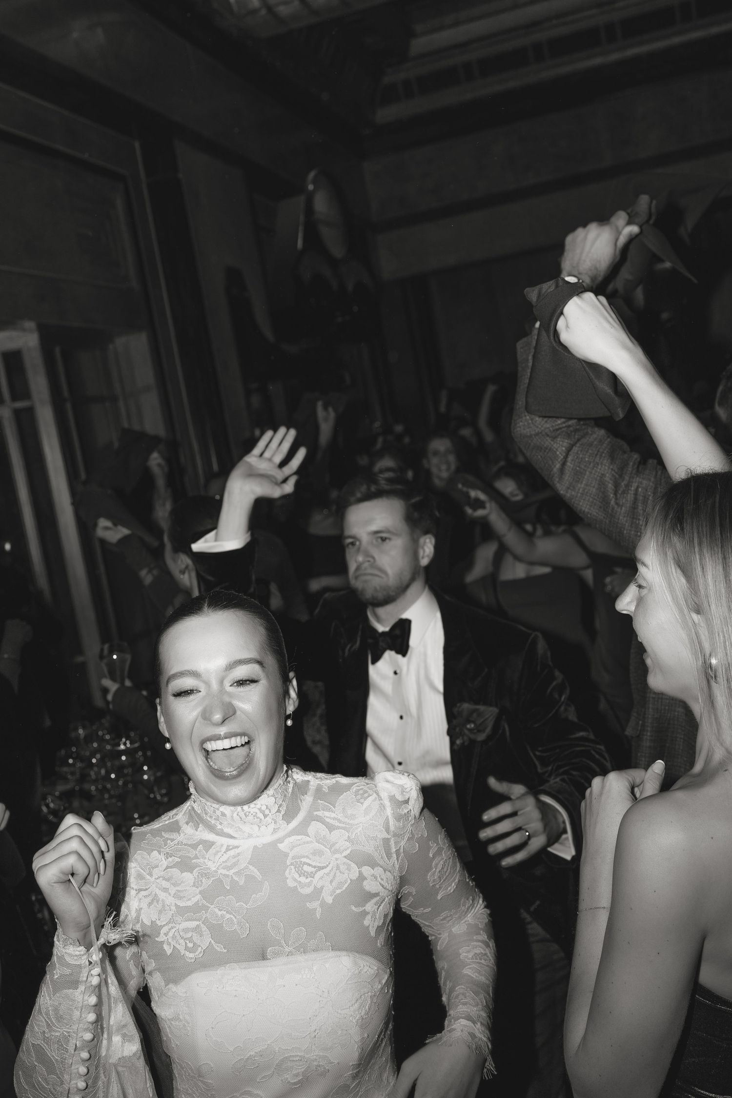 Joyful wedding celebration with guests dancing and laughing on a crowded dance floor.