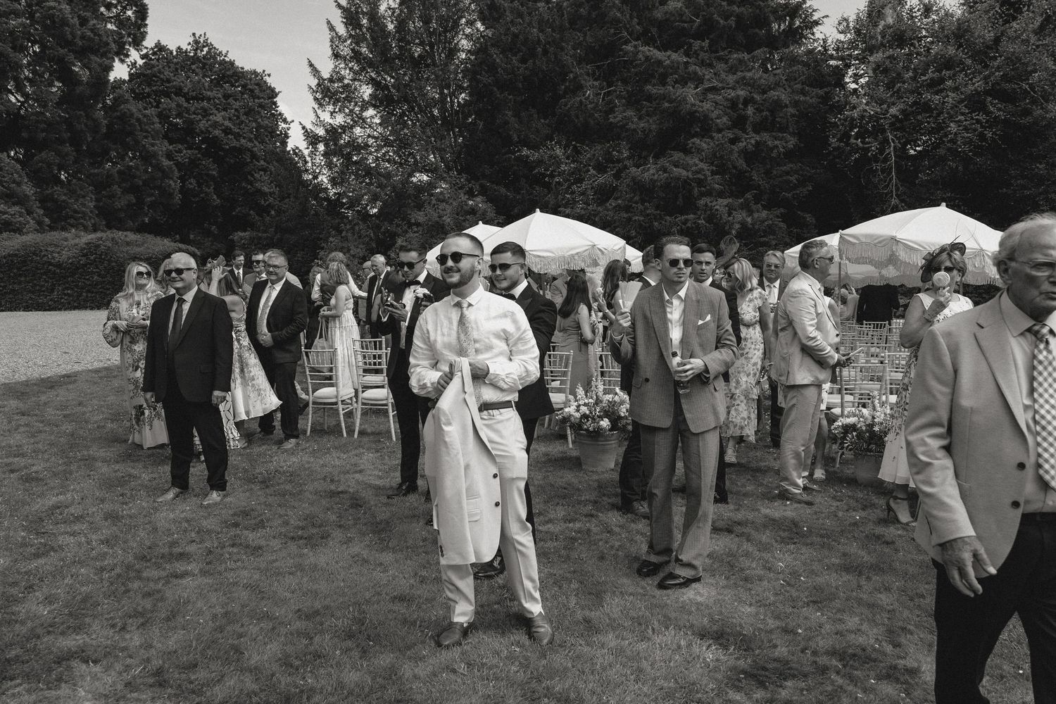 A black and white photo of wedding guests gathered outdoors under white tents during a reception.