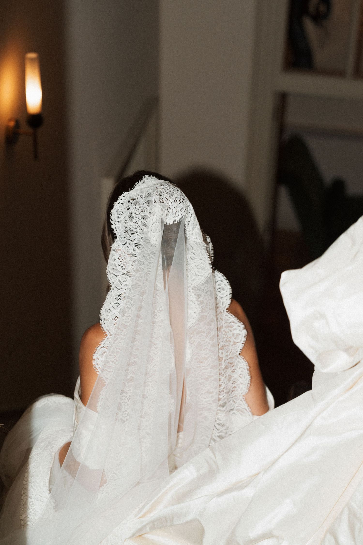 Bride seen from behind wearing a delicate lace mantilla veil over her hair with a white wedding gown flowing in the foreground.