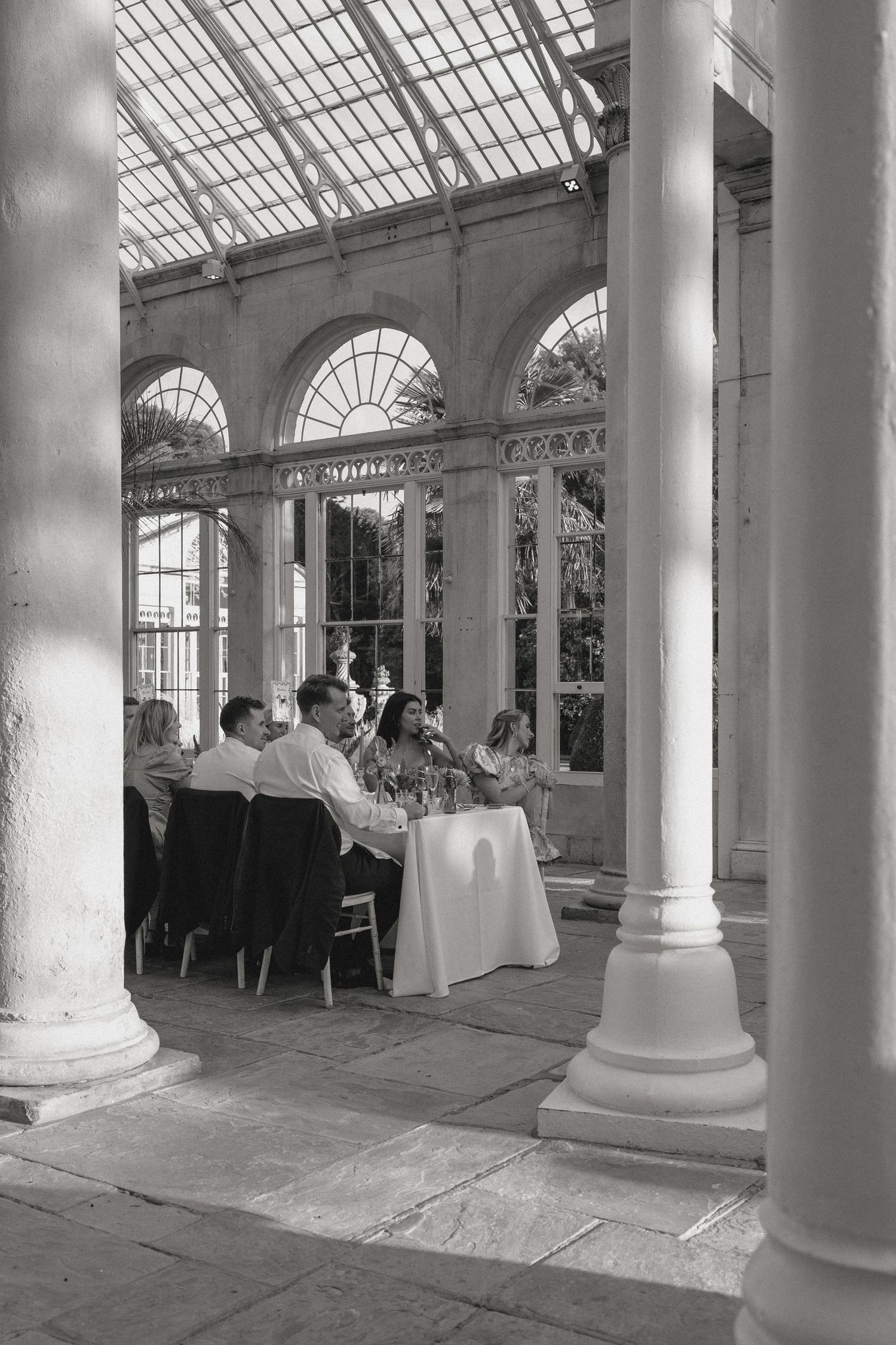 Sunlit conservatory with classical white columns and glass ceiling hosting an elegant event.