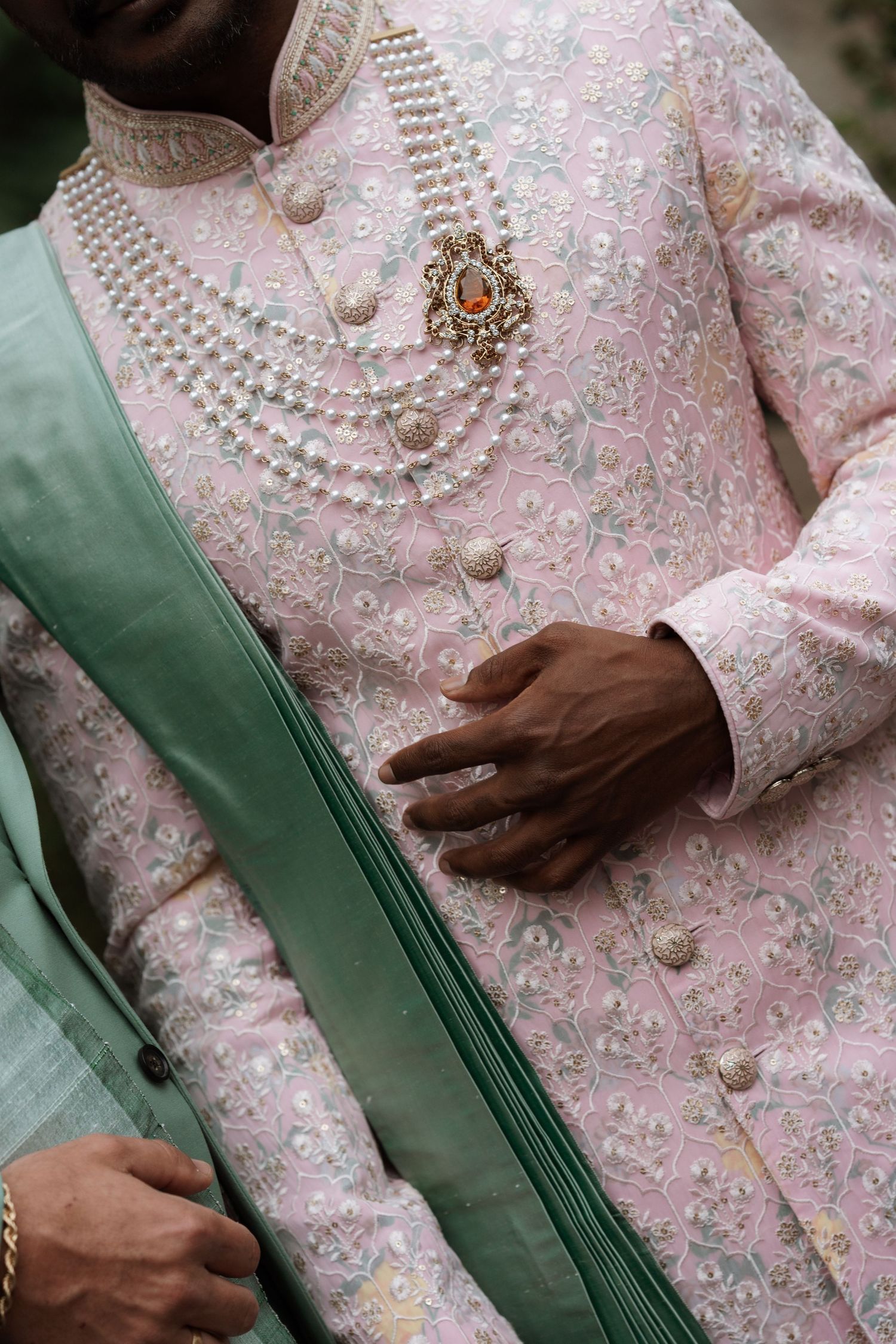 Detailed shot of pink embroidered sherwani with pearl buttons and green accents.