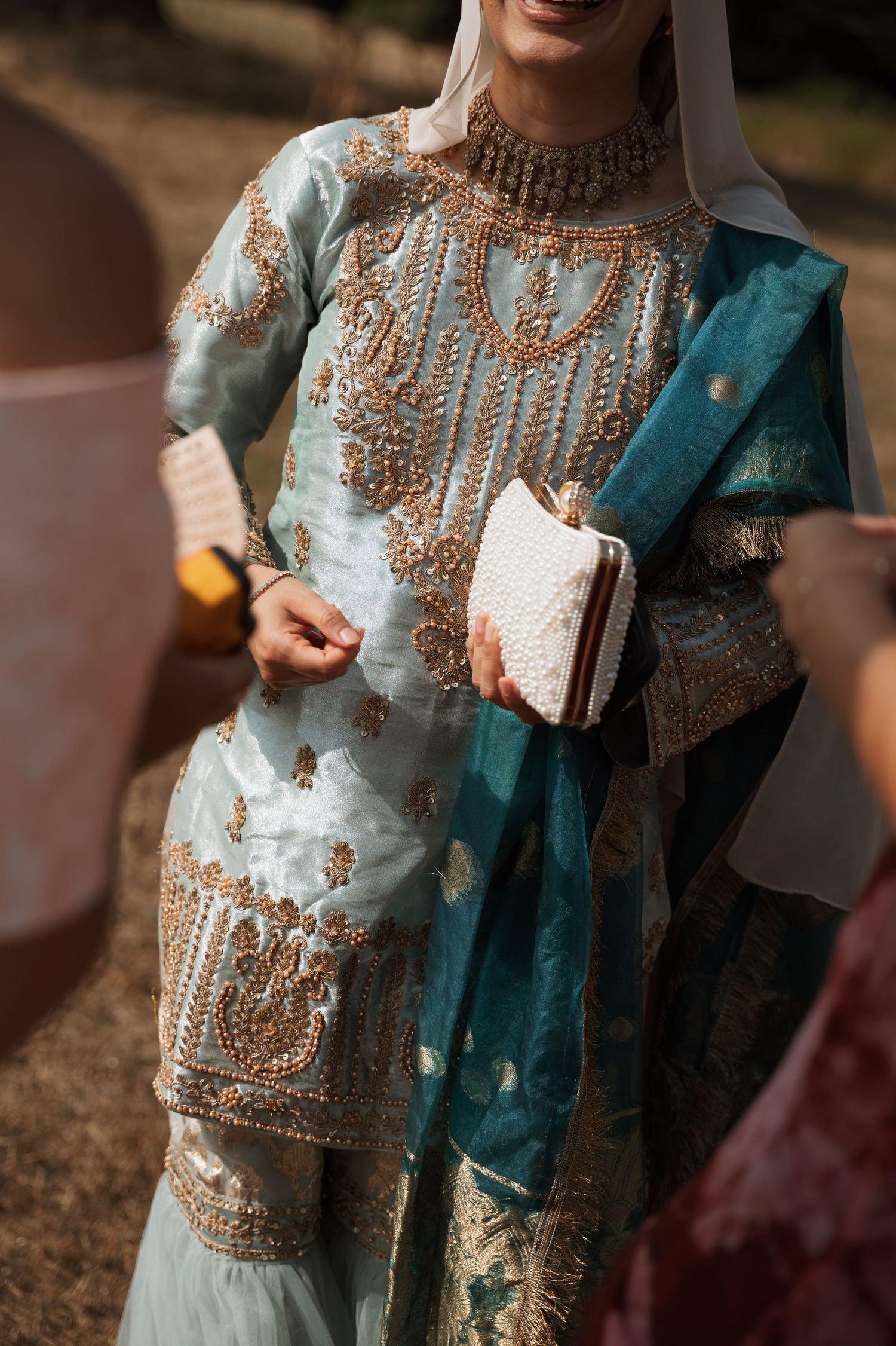 Close-up detail of intricate beadwork on a turquoise and gold traditional wedding outfit.