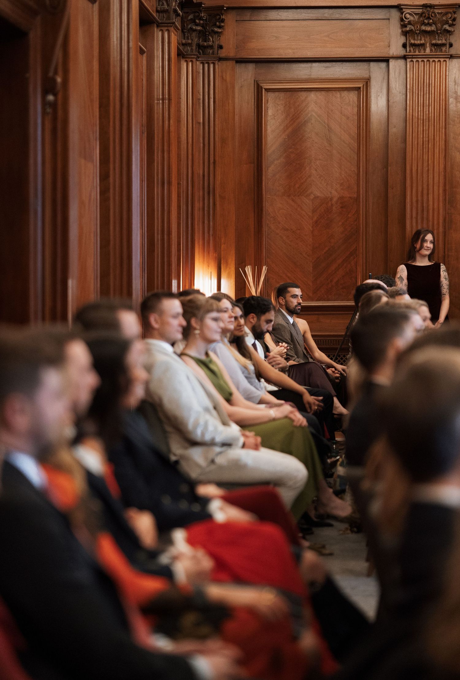 Guests seated in wood-paneled auditorium with ornate architectural details during formal event.
