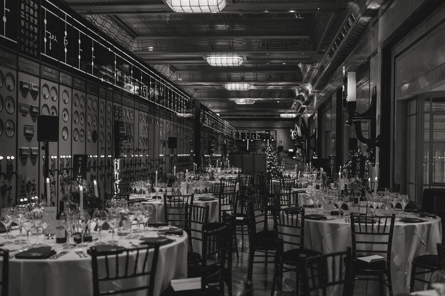 Large dining room with round tables set for formal dinner under industrial ceiling.