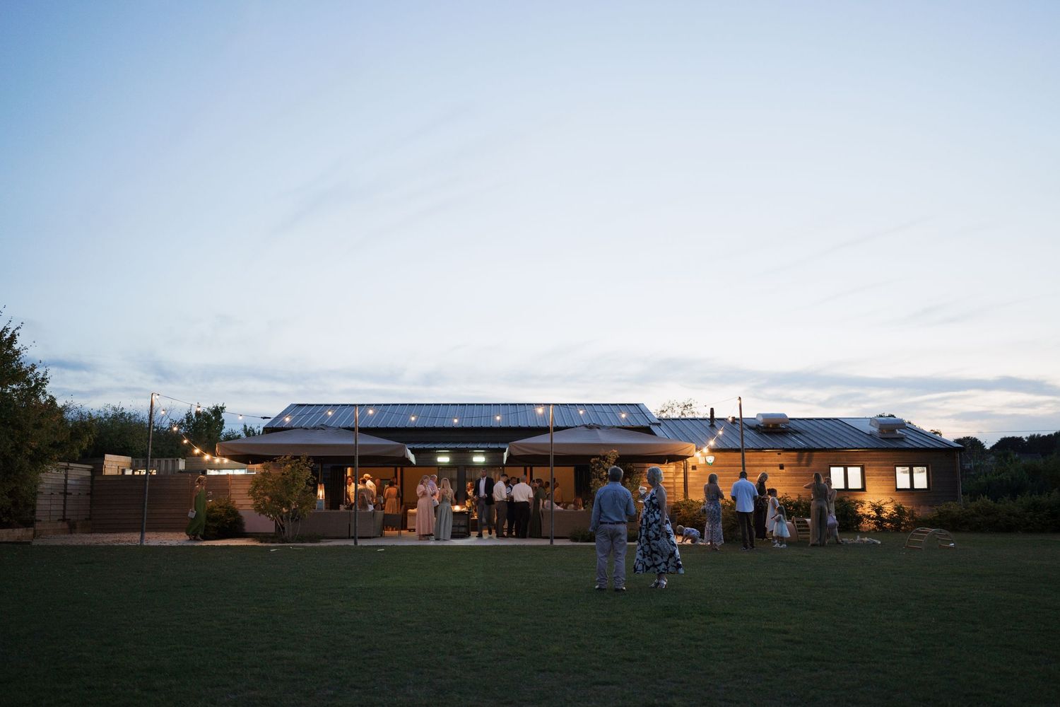 Wedding venue at dusk with warm lighting and guests mingling on outdoor lawn.