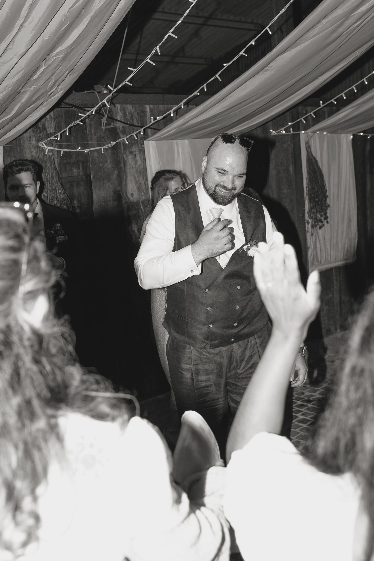 Black and white photo of a groom dancing at his wedding reception under string lights and draped fabric.