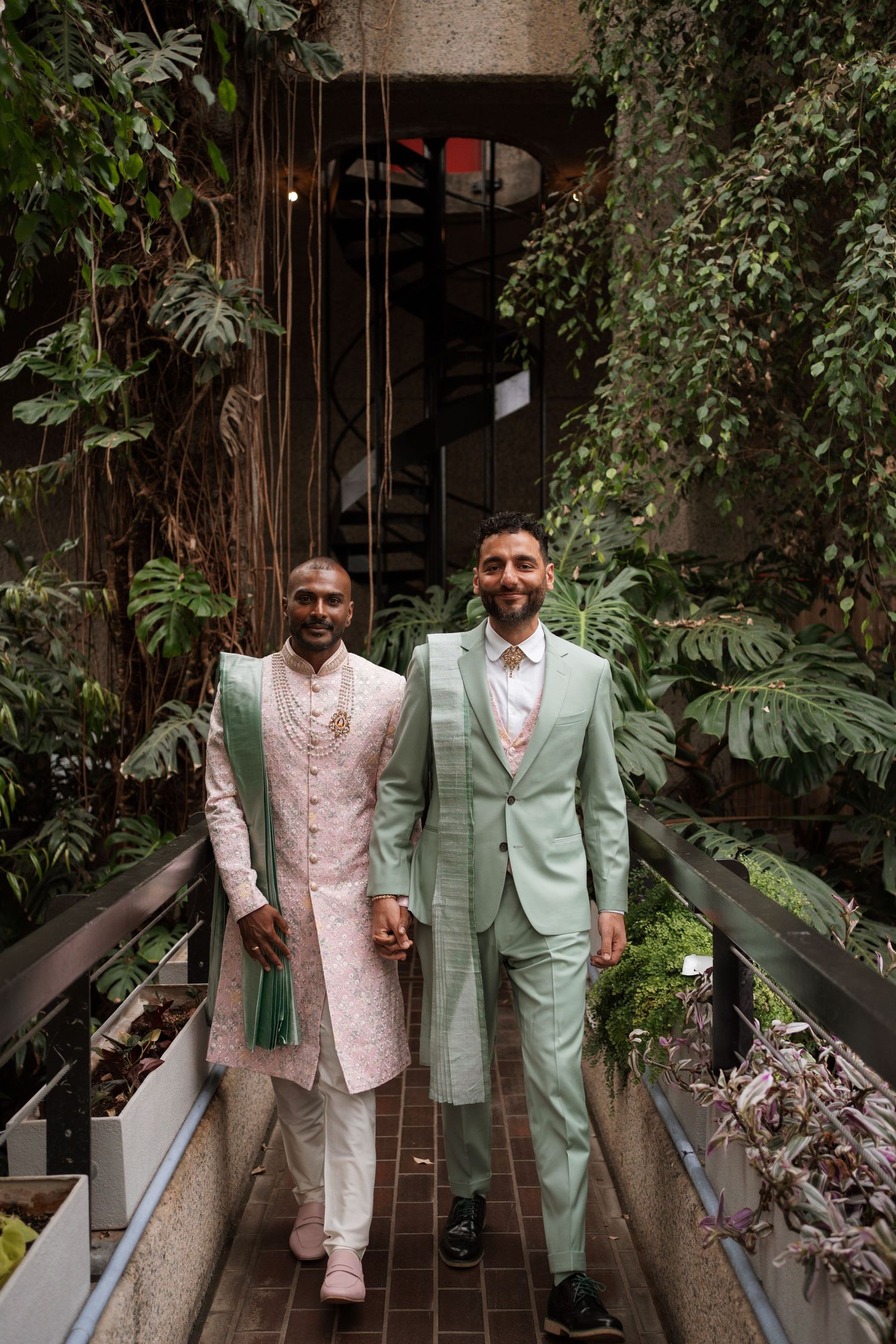 Wedding party poses in stylish pink and mint green suits in a greenhouse setting.