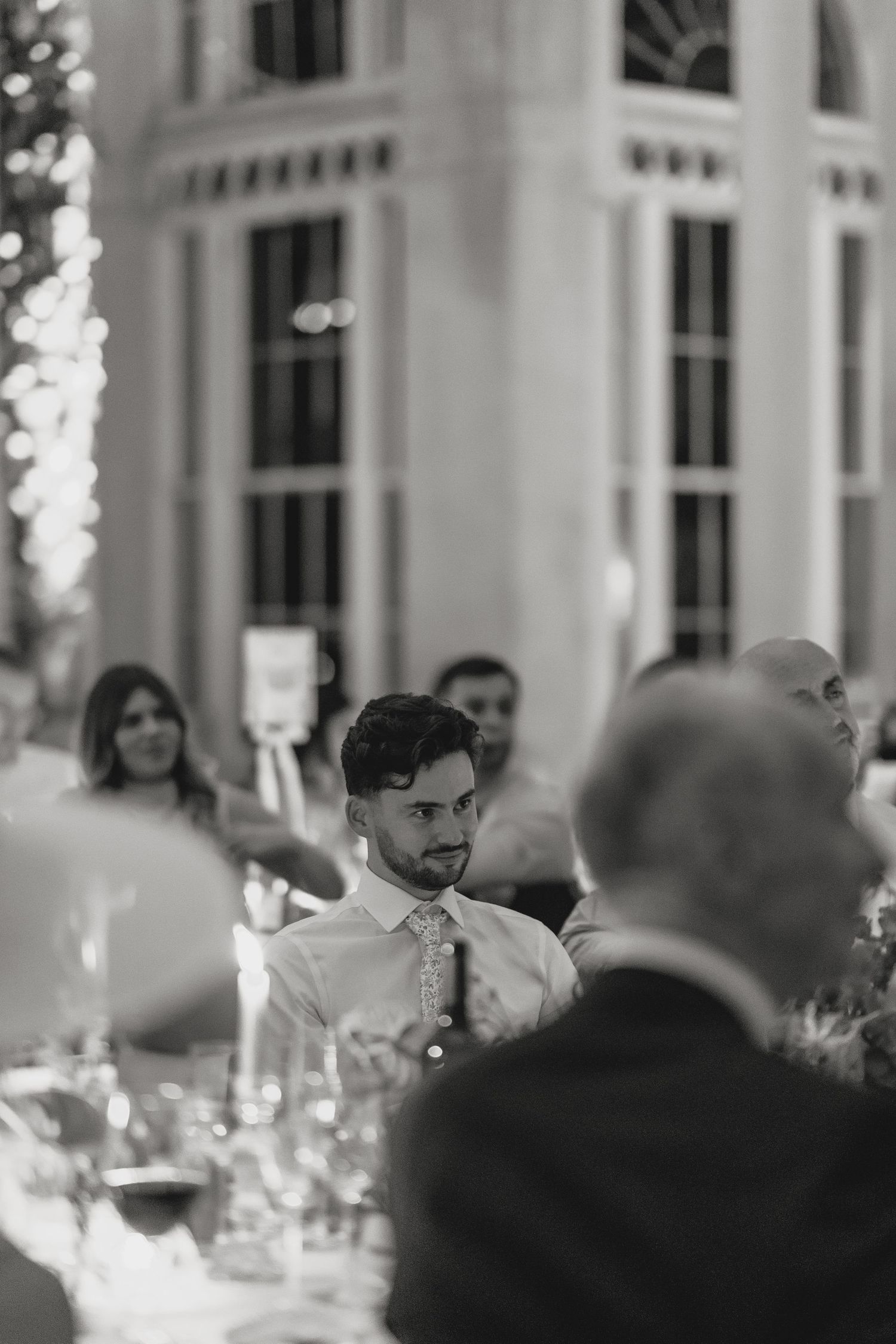 Candid black and white shot of wedding guests during dinner reception.