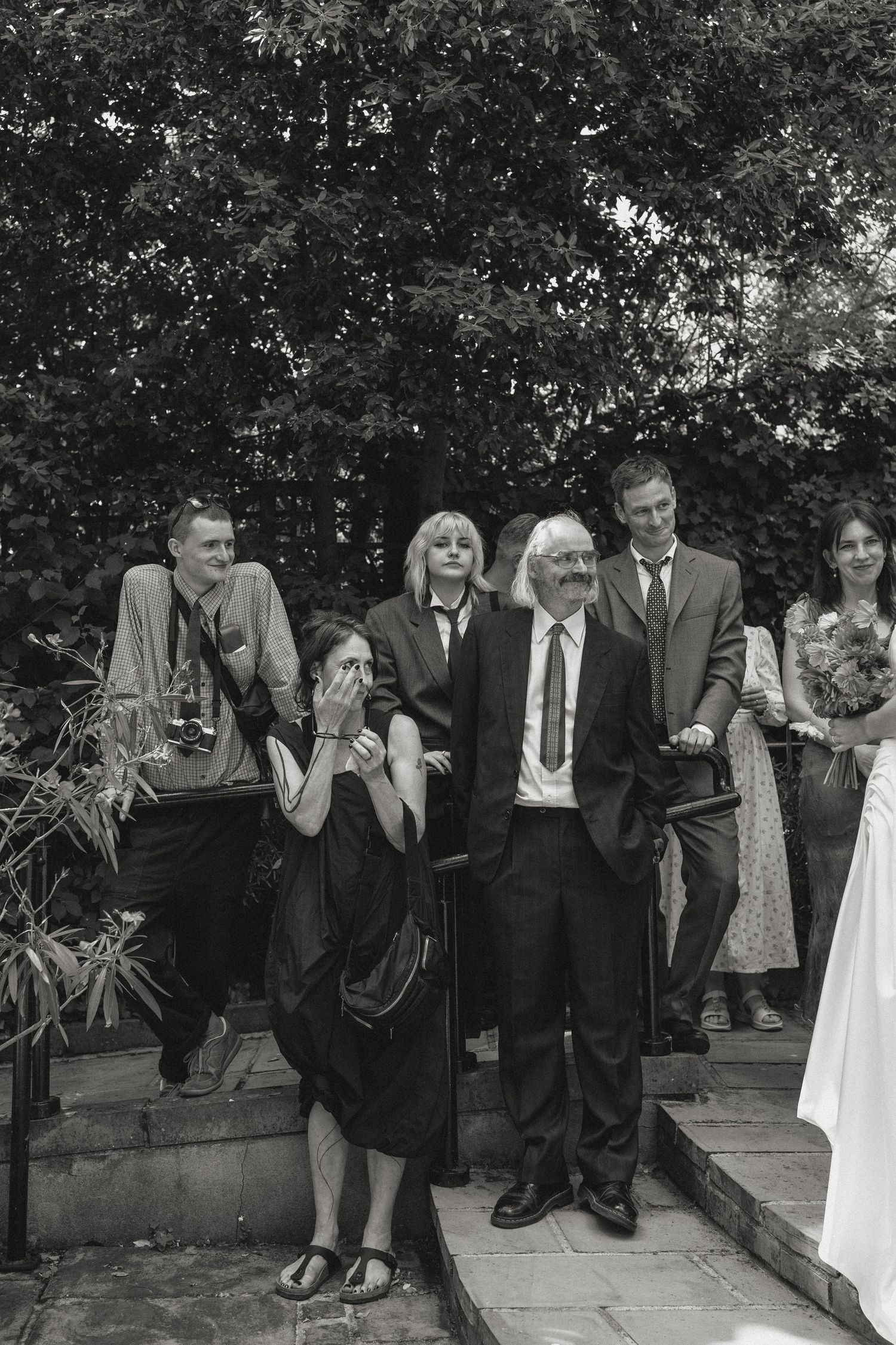 Black and white photo of wedding guests seated casually on outdoor stone steps.