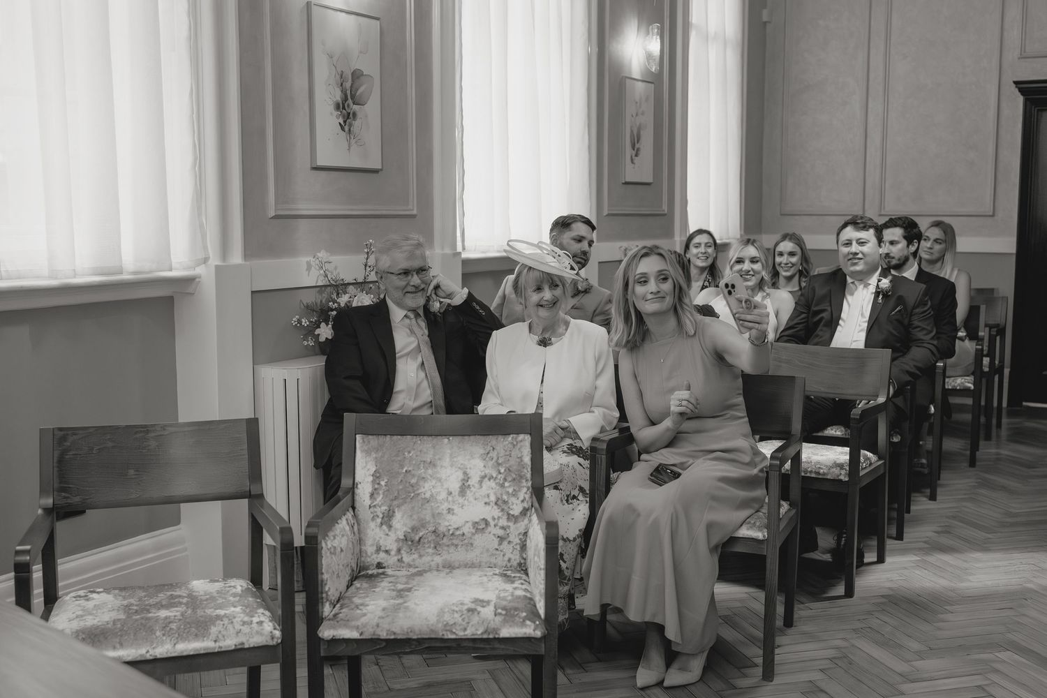 Guests seated in elegant chairs at a wedding ceremony, smiling and celebrating in a classic interior.