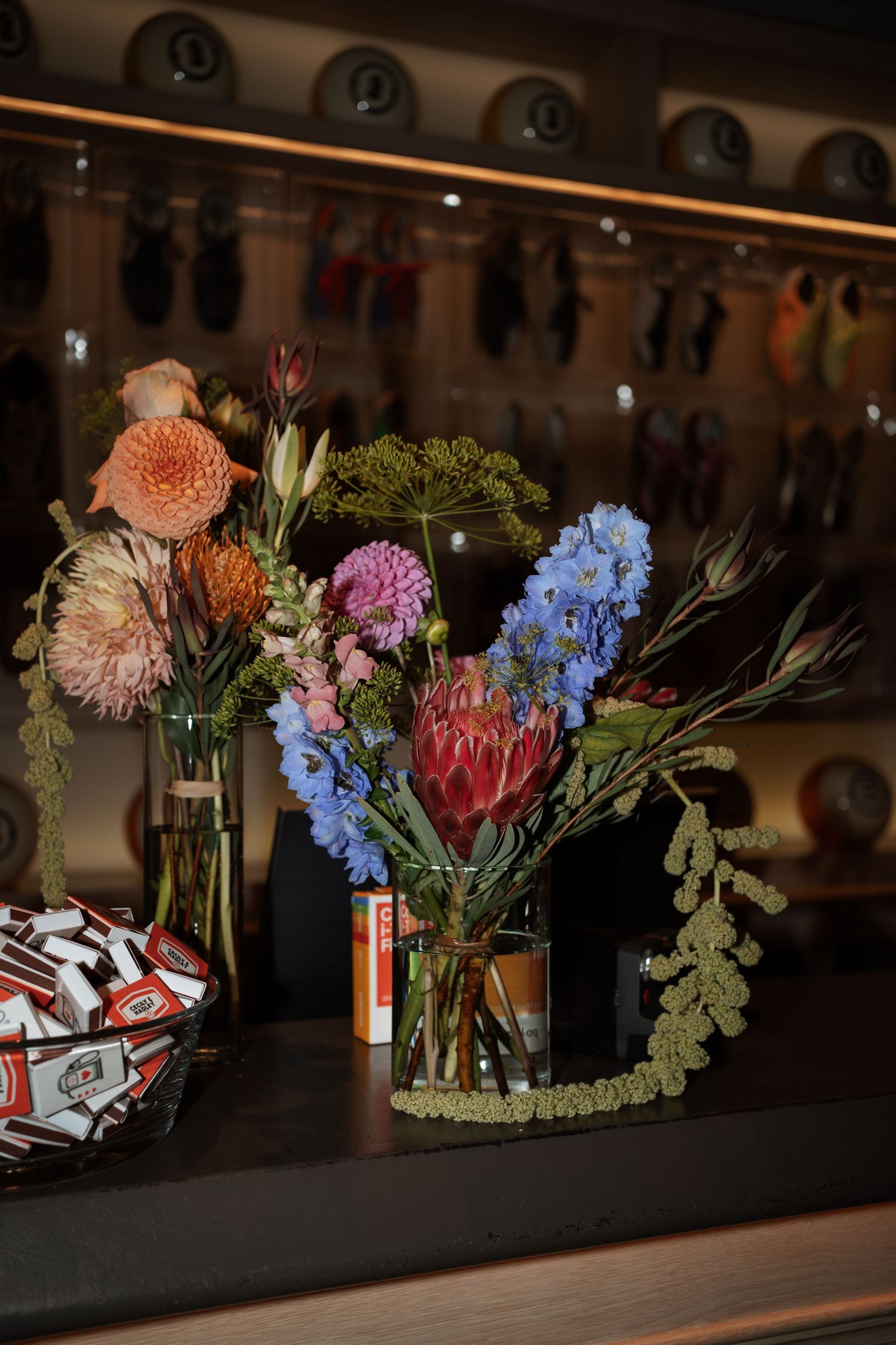 Colorful floral arrangements with protea, dahlias and blue hydrangeas on a dark surface.