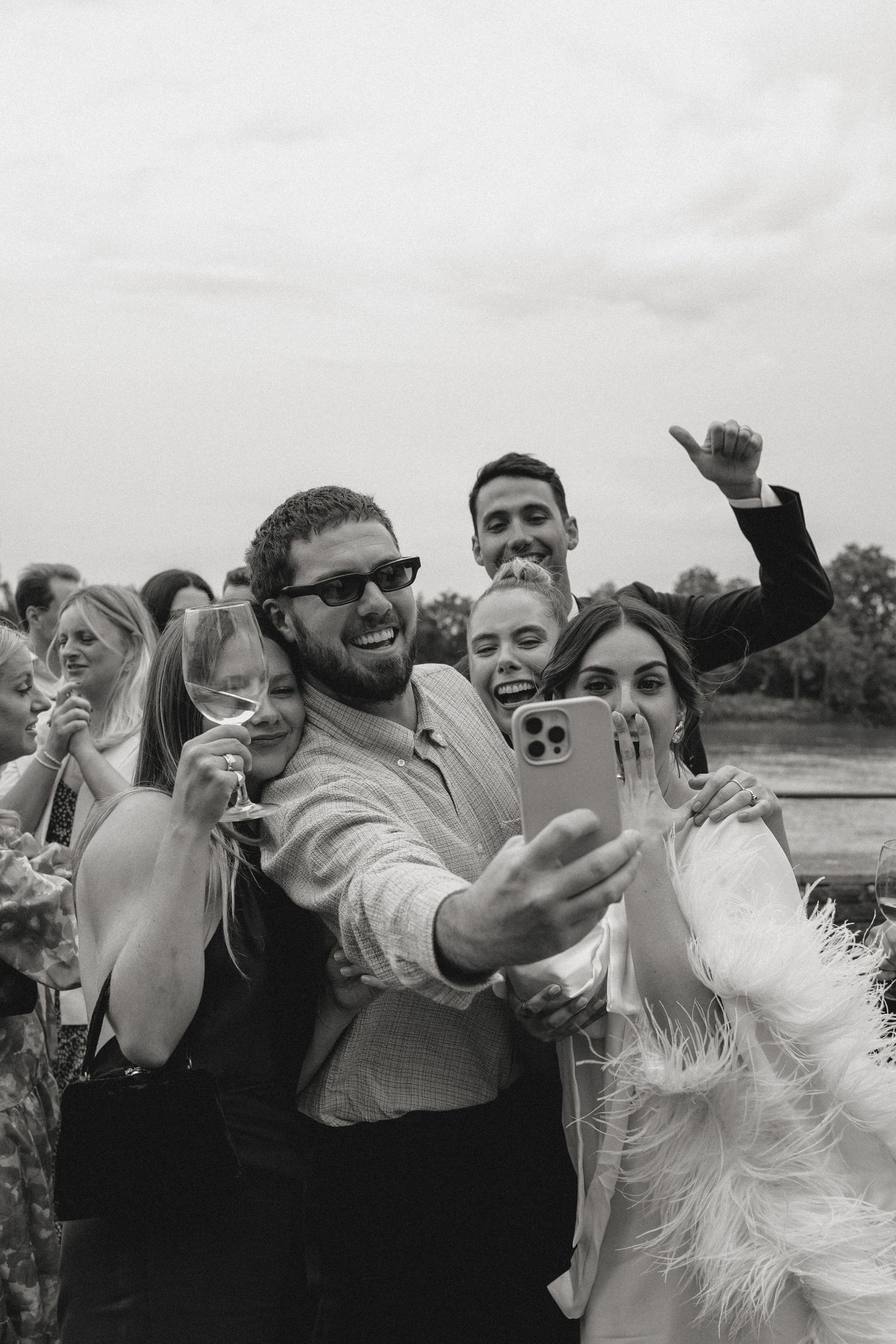 Joyful wedding party celebrates outdoors with energetic poses against a natural backdrop.