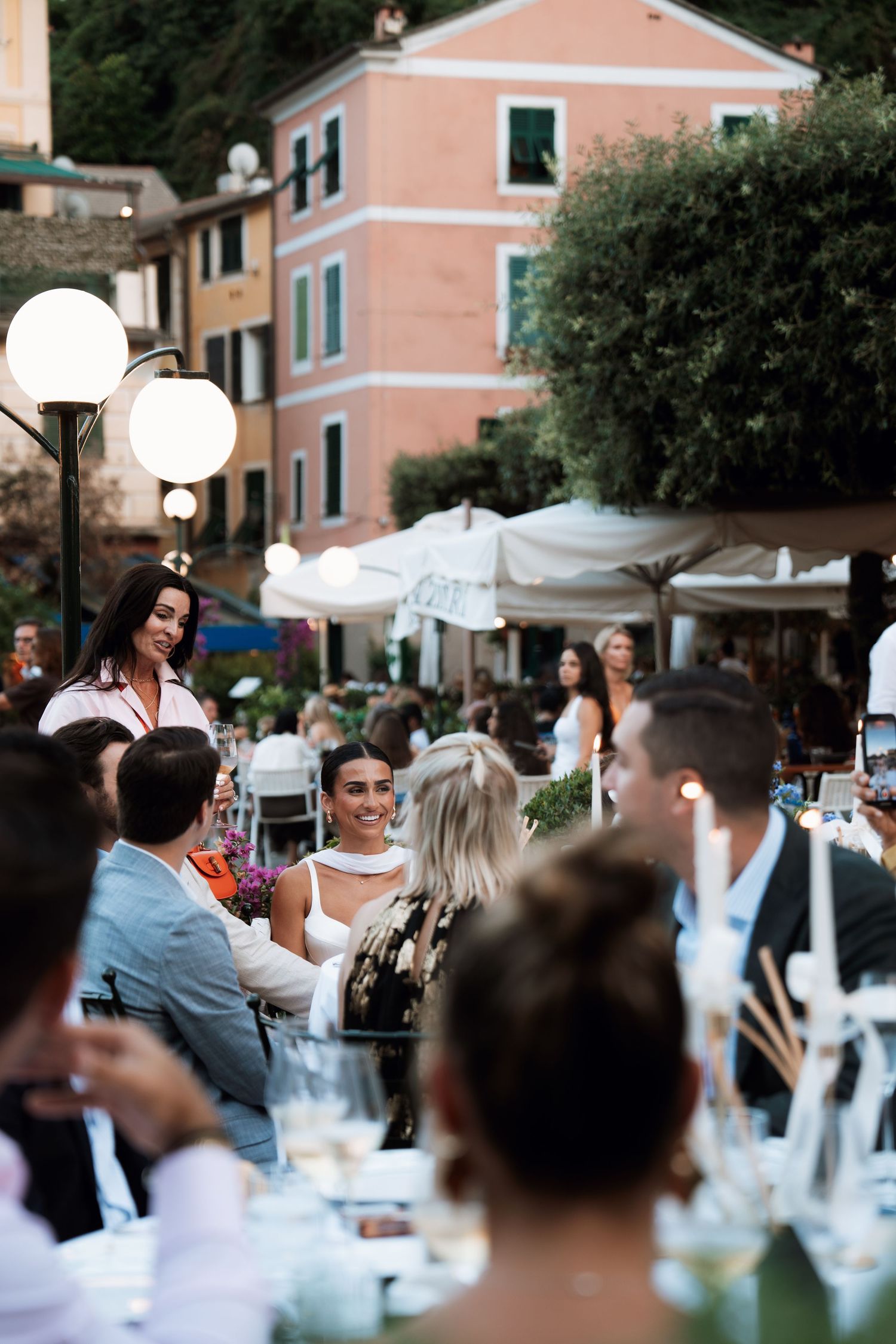 Outdoor dining scene with pink buildings and white tablecloths in a Mediterranean setting.