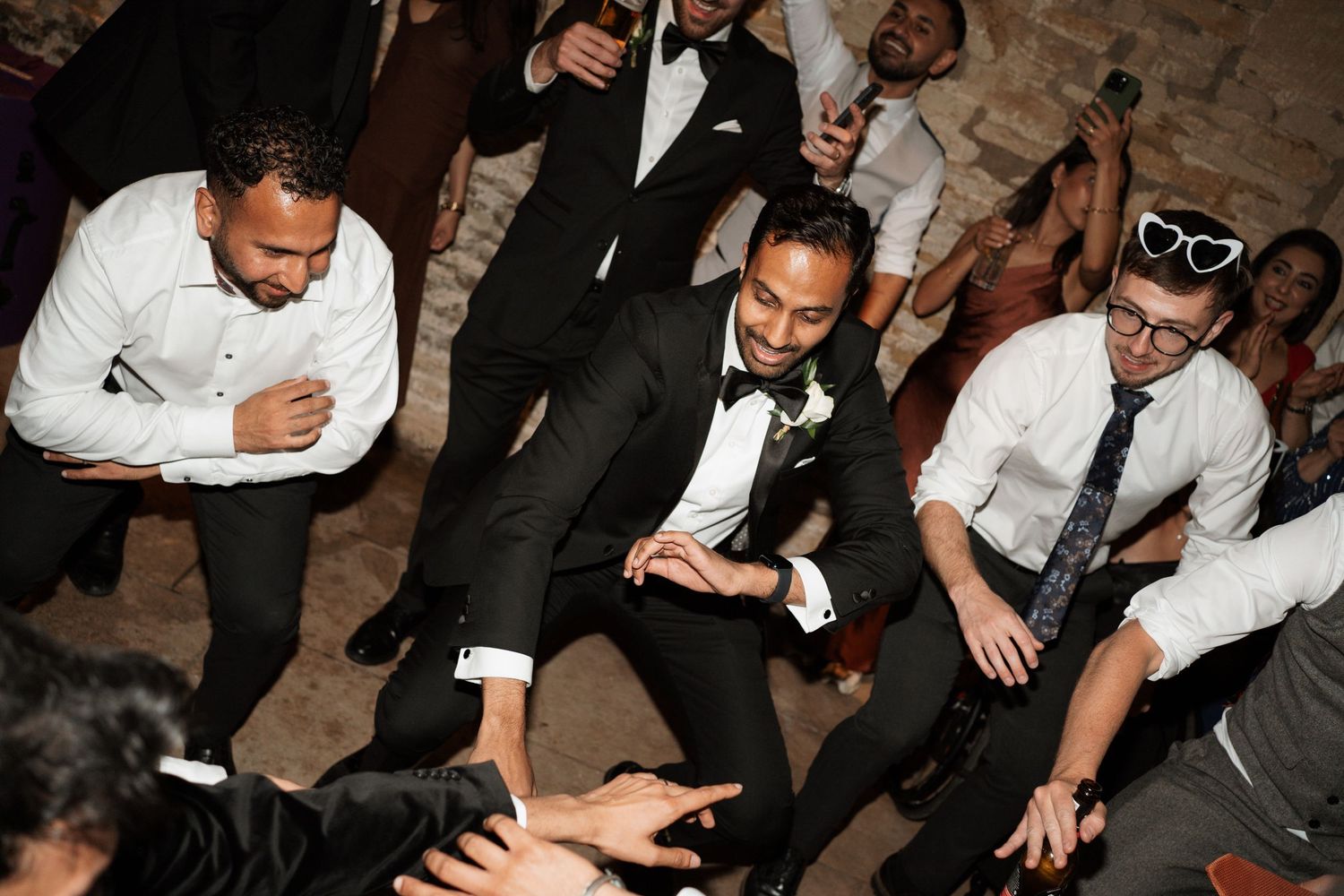 Wedding guests dancing and celebrating on dimly lit dance floor.
